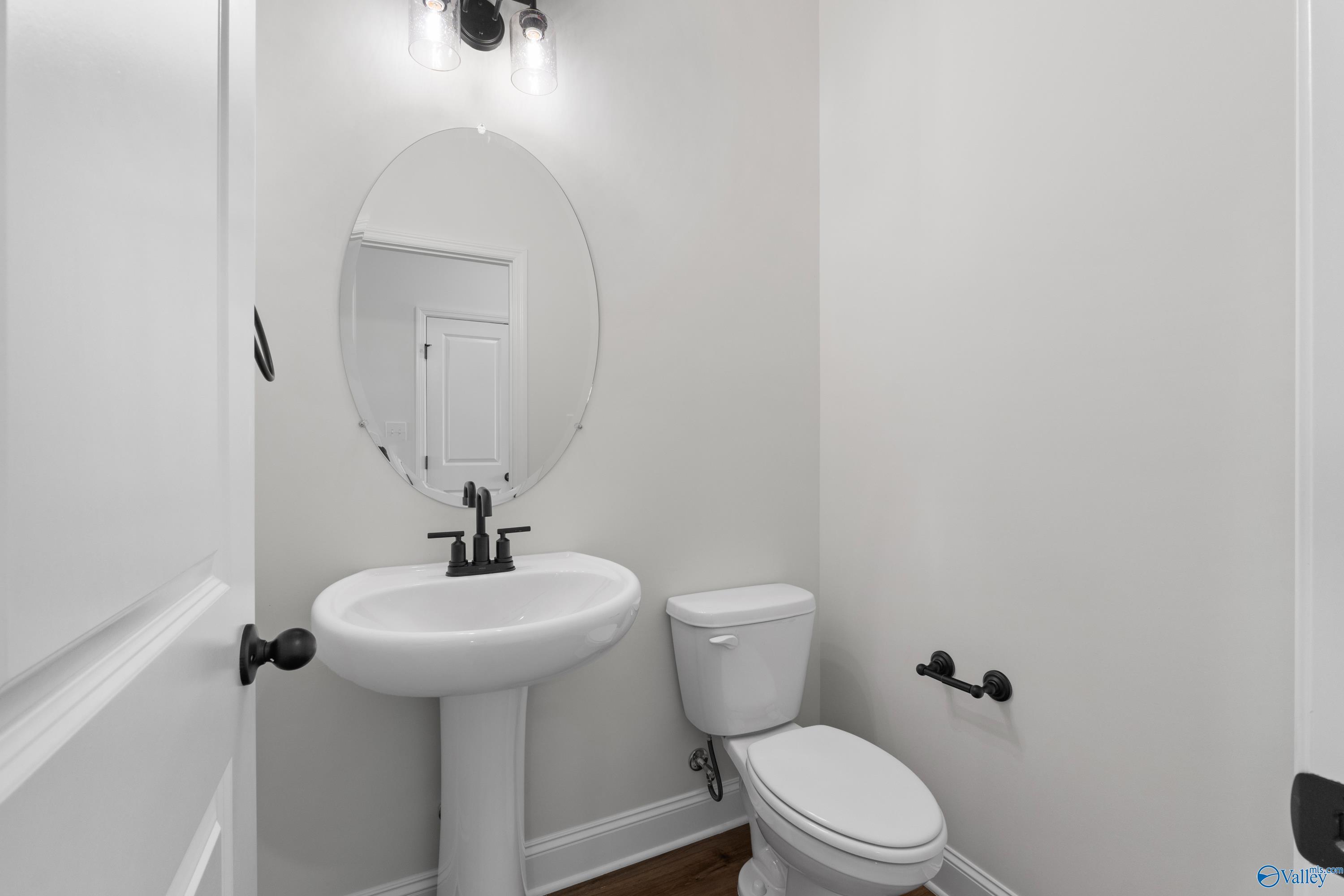 Elegant powder room with pedestal sink, round mirror, and toilet in Davidson Homes The Rockford B, Toney, Alabama