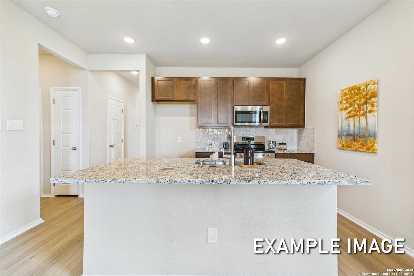 Modern kitchen featuring granite island, stainless appliances, wood cabinets in Davidson Homes The Comal B, San Antonio