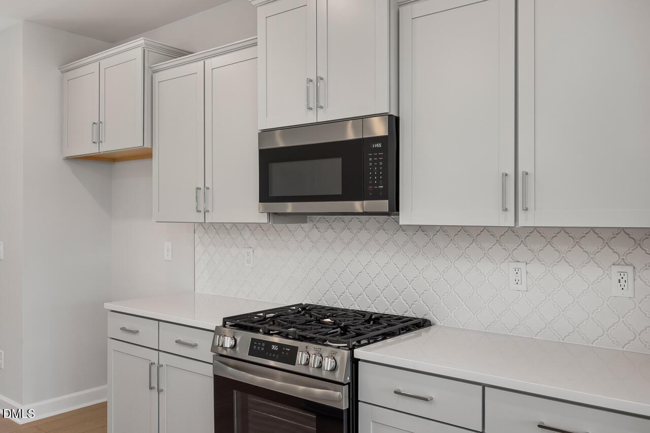 Modern kitchen with gray cabinets, gas range, and patterned backsplash in a Davidson Homes house at Camden Park, Knightdale.