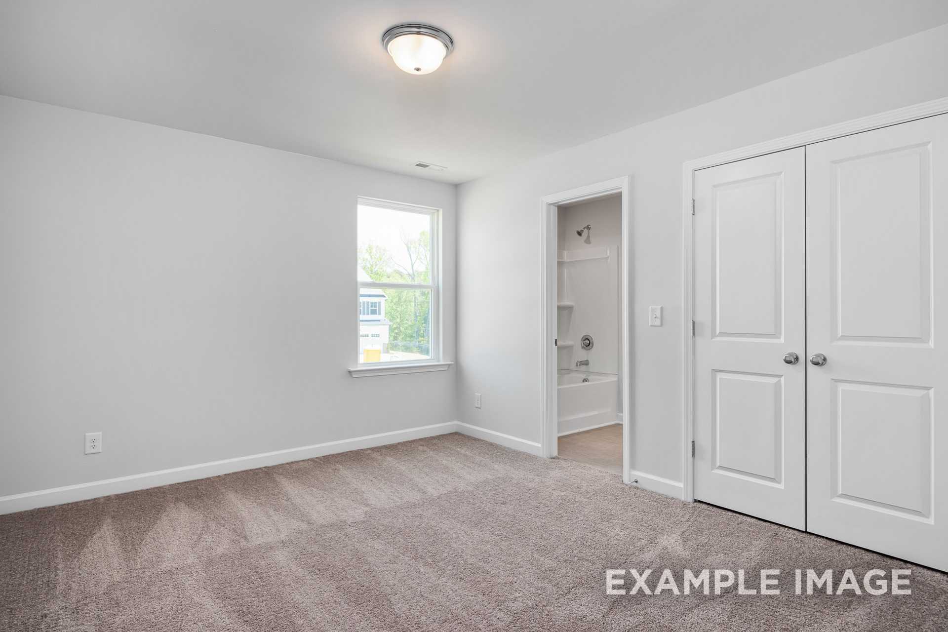 Spacious upper-floor bedroom in The Gavin C home with light gray walls, beige carpet, large window, walk-in closet, and en-suite bath