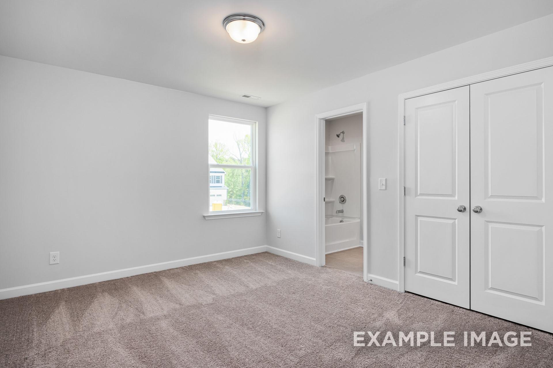 Spacious master bedroom in The Gavin B featuring walk-in closet, en-suite bath, beige carpet, and window light