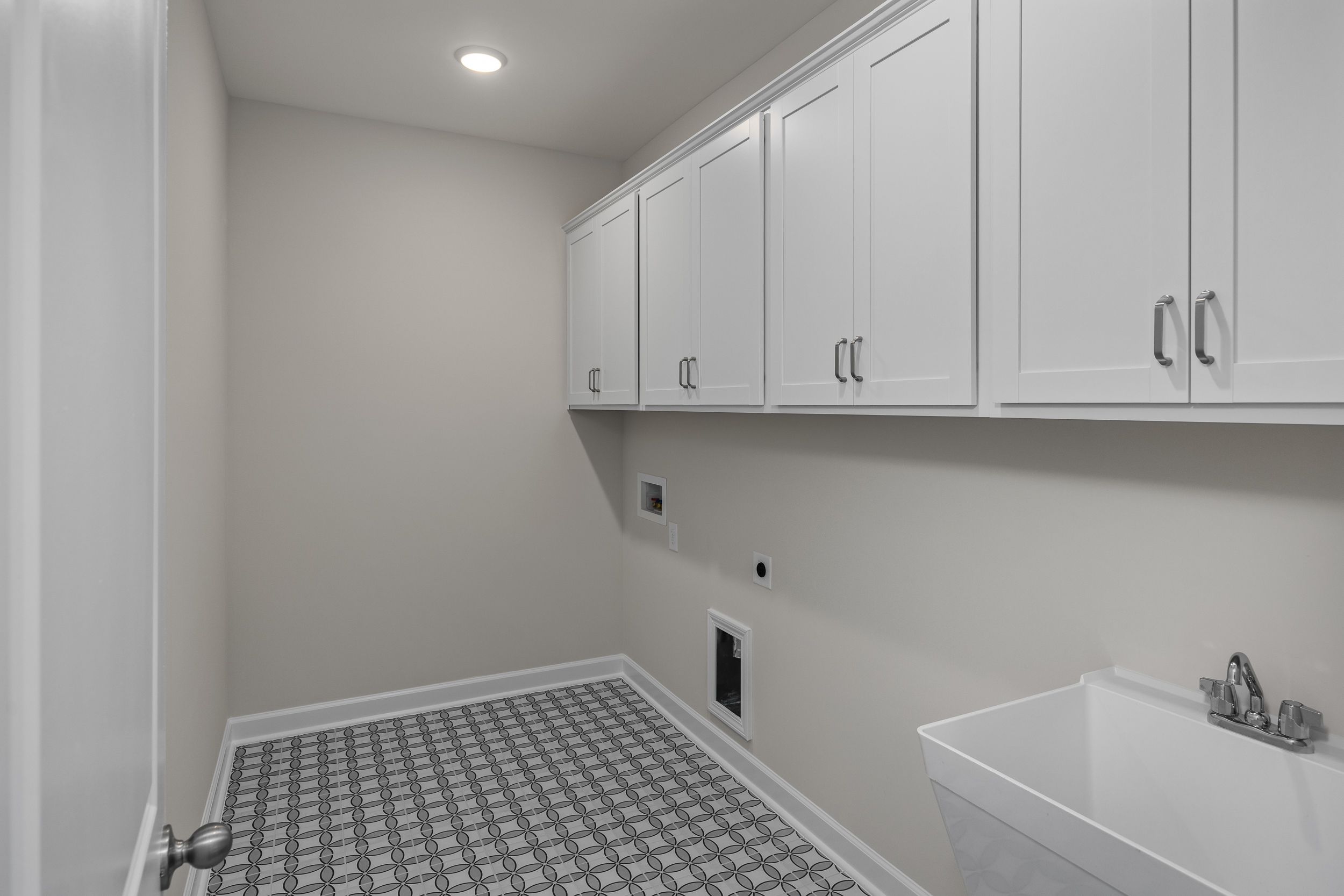 Spacious laundry room in The Aspen by Davidson Homes with white upper cabinets, utility sink, washer-dryer hookups, and gray checkered tile floor