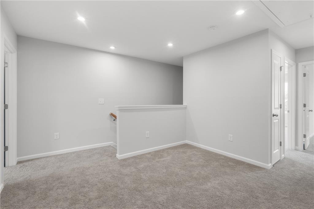 Spacious upstairs loft with beige carpet, light gray walls, recessed lights, and wooden railing in Davidson Homes The Monroe B, Emerson, Georgia
