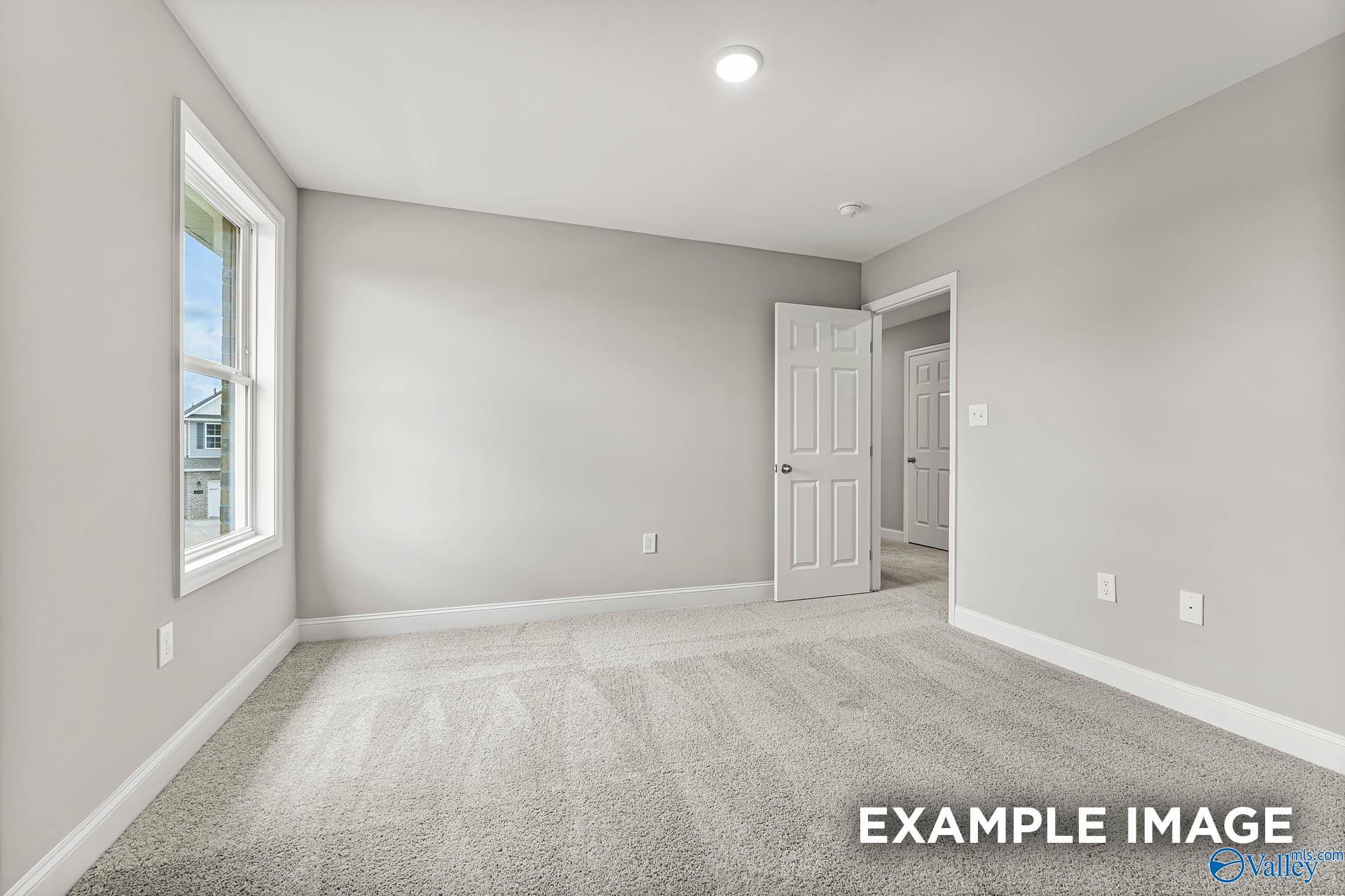 Empty bedroom with light gray walls, large window overlooking homes, open door, and beige carpet in Davidson Homes Chelsea B, Toney, Alabama