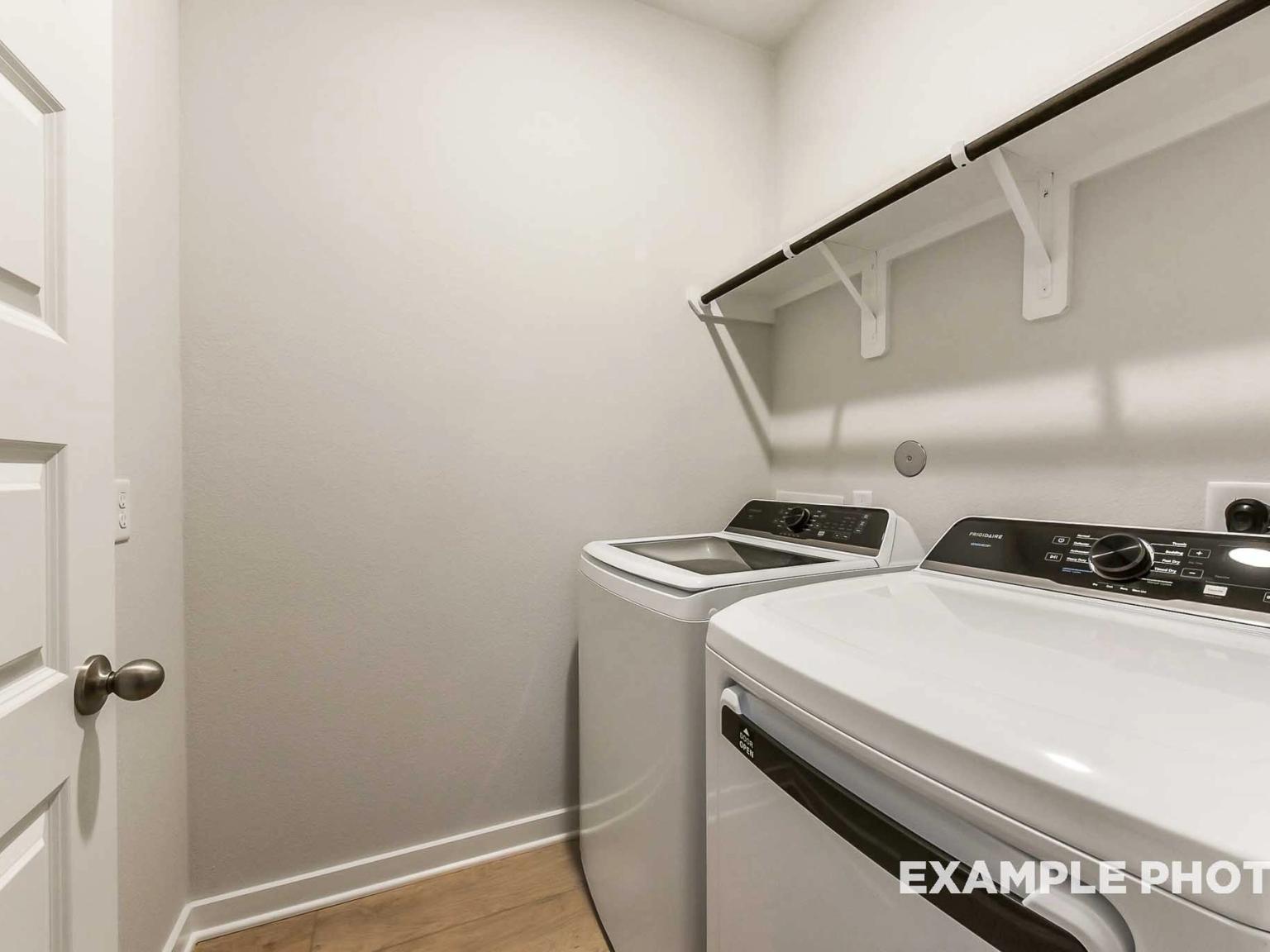 Laundry room with washer and dryer and overhead shelving in The Brookside F floor plan at Enclave at Newport, Crosby, TX.
