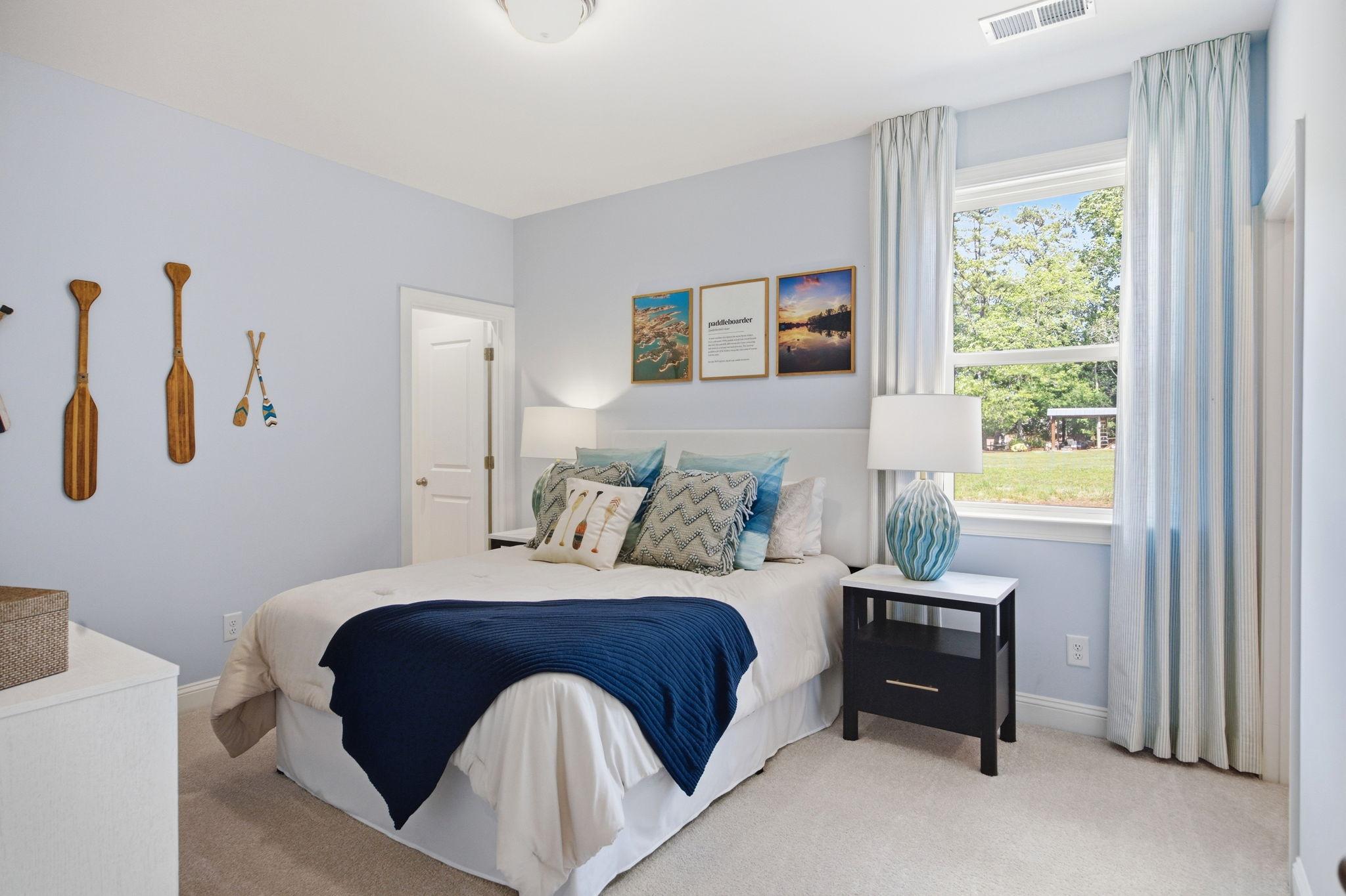 Serene bedroom at Enclave at Belmont in Belmont NC by Davidson Homes with light blue walls, nautical oar decor, queen bed and window view