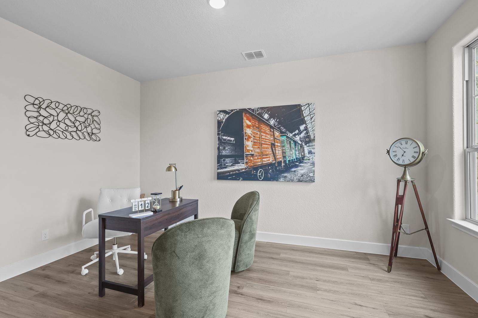 Modern home office in The Belmont J featuring a dark wood desk, velvet chairs, and industrial wall art decor.
