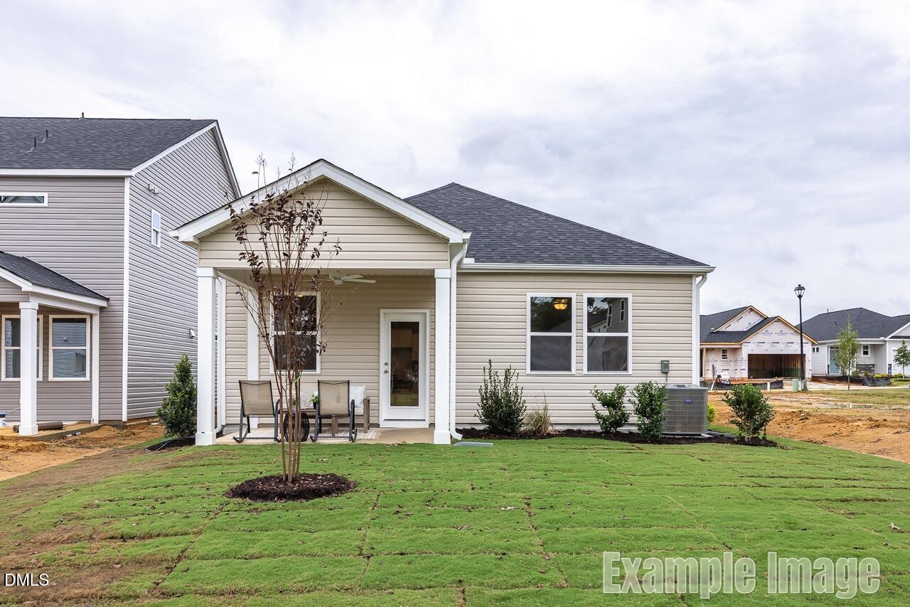 Modern beige one-story home with covered front porch, young tree, and sod yard in Gregory Village, Lillington, NC - Davidson Homes Carter C