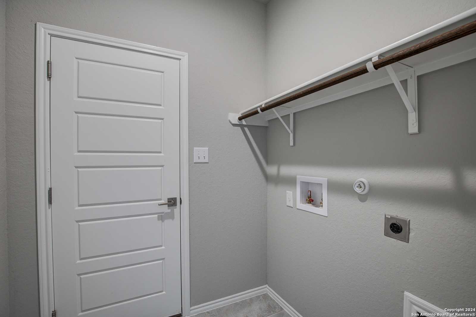 Functional laundry room with utility sink, wooden shelving, and gray walls in Davidson Homes The Frio B, San Antonio, Texas