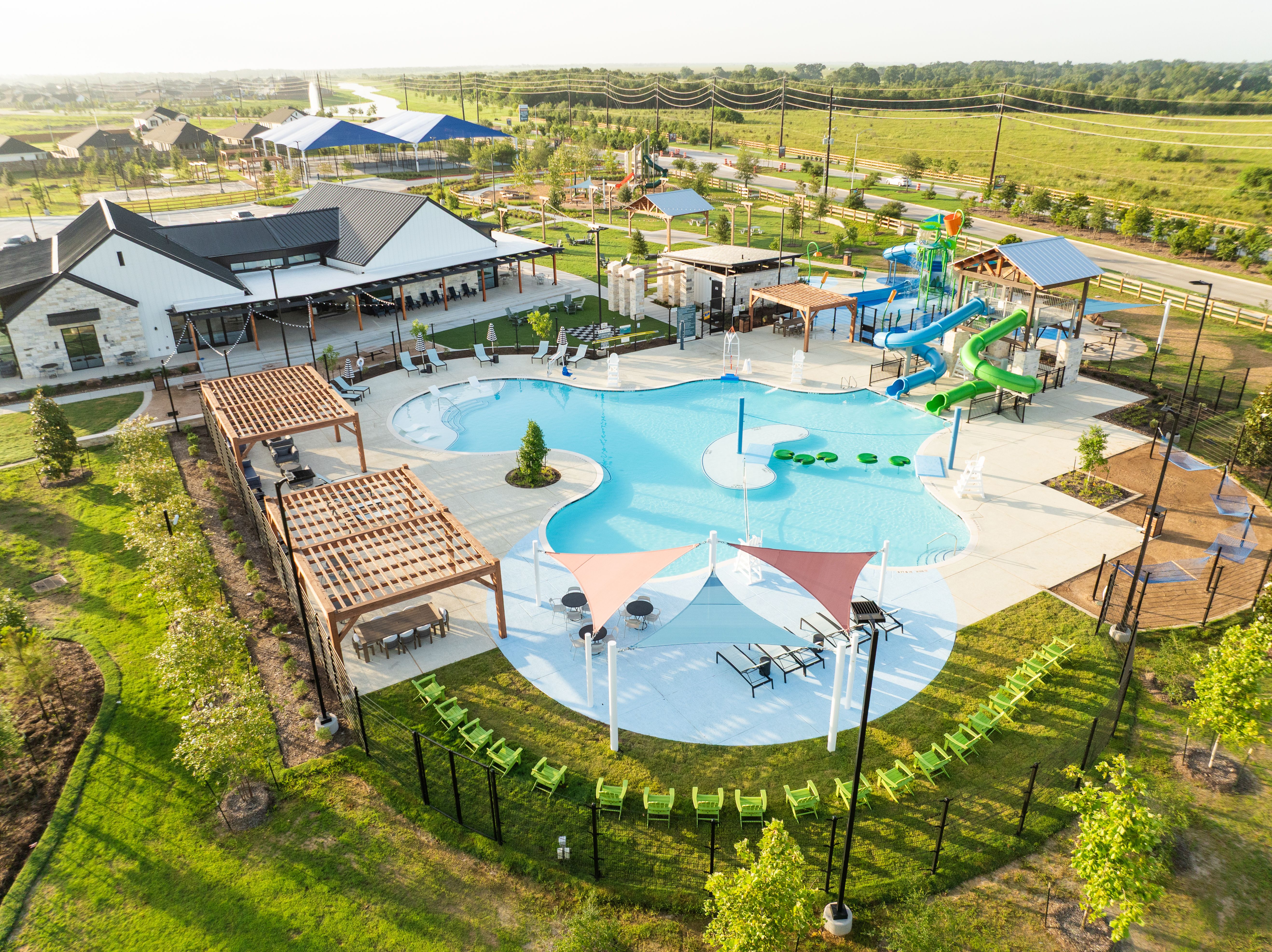 Resort-style pool at Emberly in Beasley Texas with green water slides splash pads cabanas lounge seating and green lawns