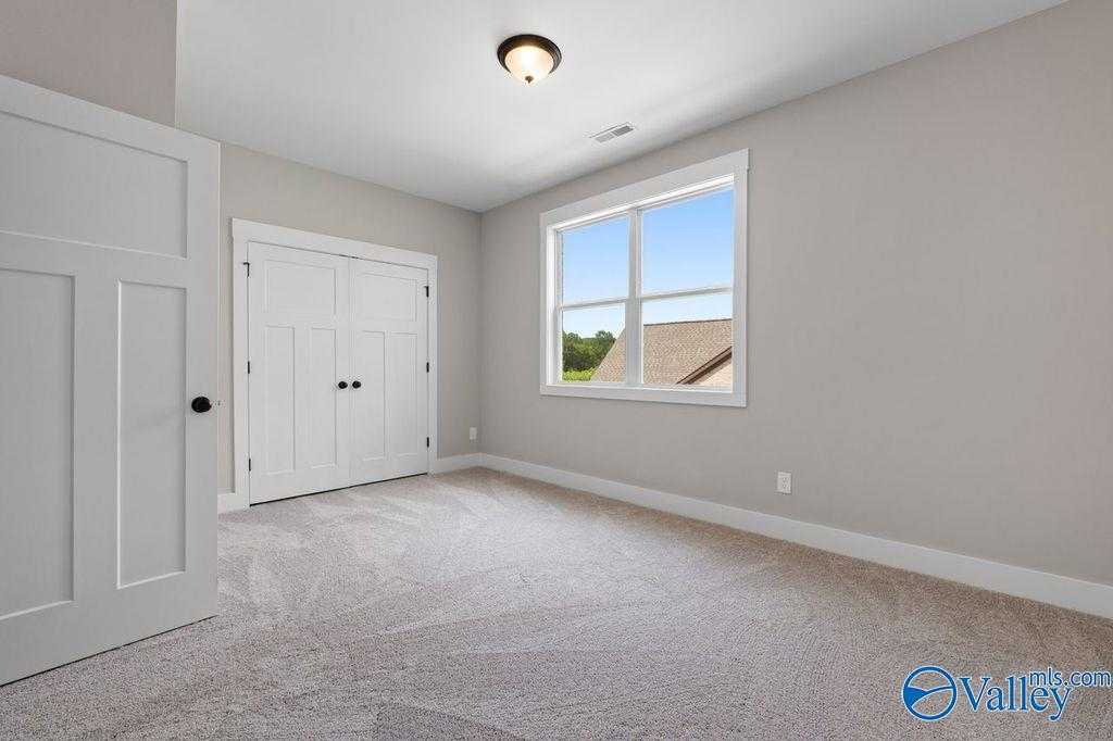 Bright secondary bedroom with large window, neutral carpet, and double doors in Evermore Homes The Oxford, Owens Cross Roads, Alabama