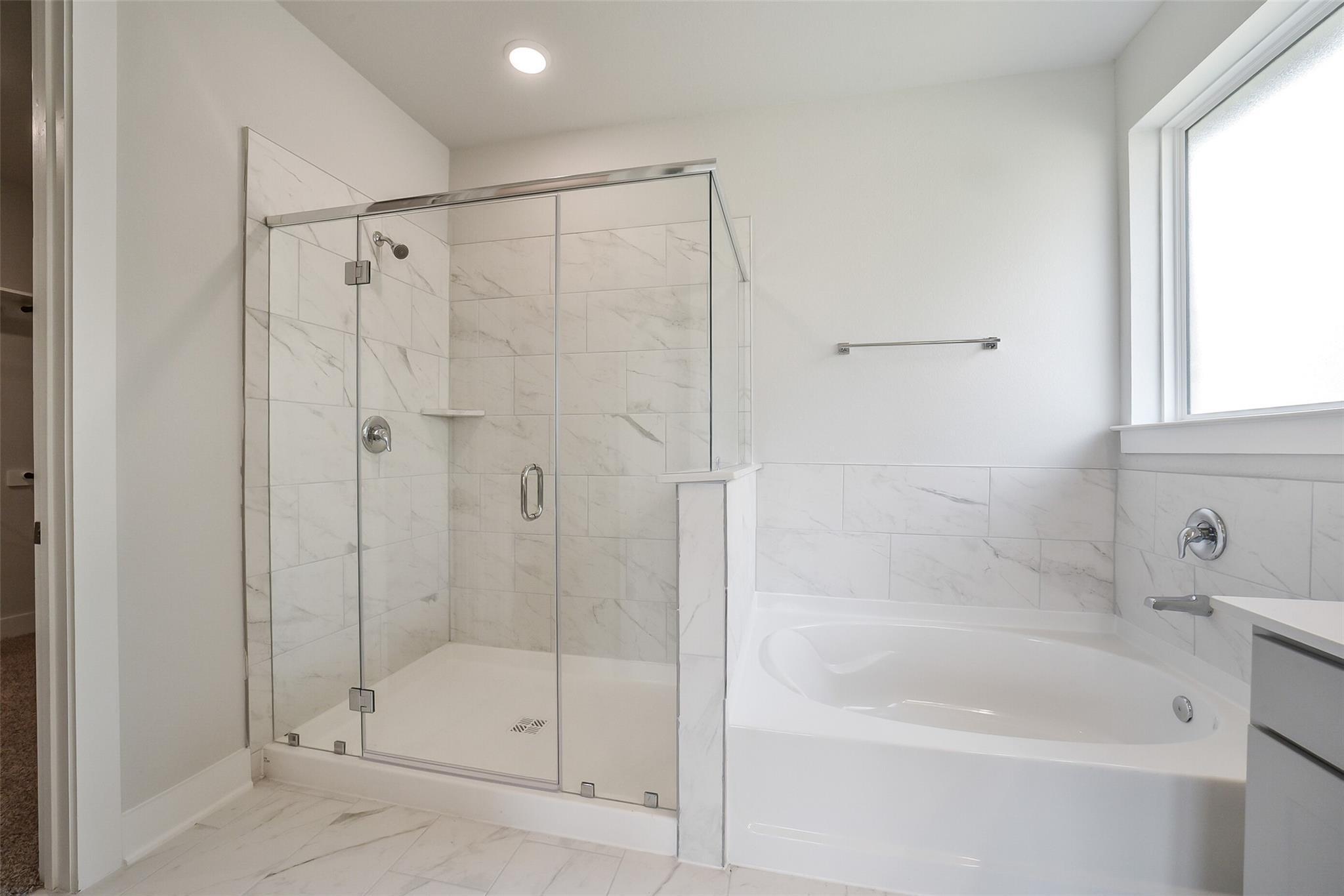 Modern master bathroom featuring frameless glass shower, white tile, and soaking tub in Davidson Homes The Philip B, Rosharon, Texas