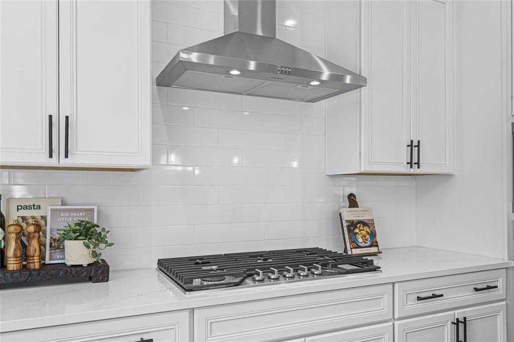 Modern white kitchen with shaker cabinets, stainless steel hood, 6-burner gas cooktop, subway tile backsplash in Davidson Homes Hickory B, Hoschton GA