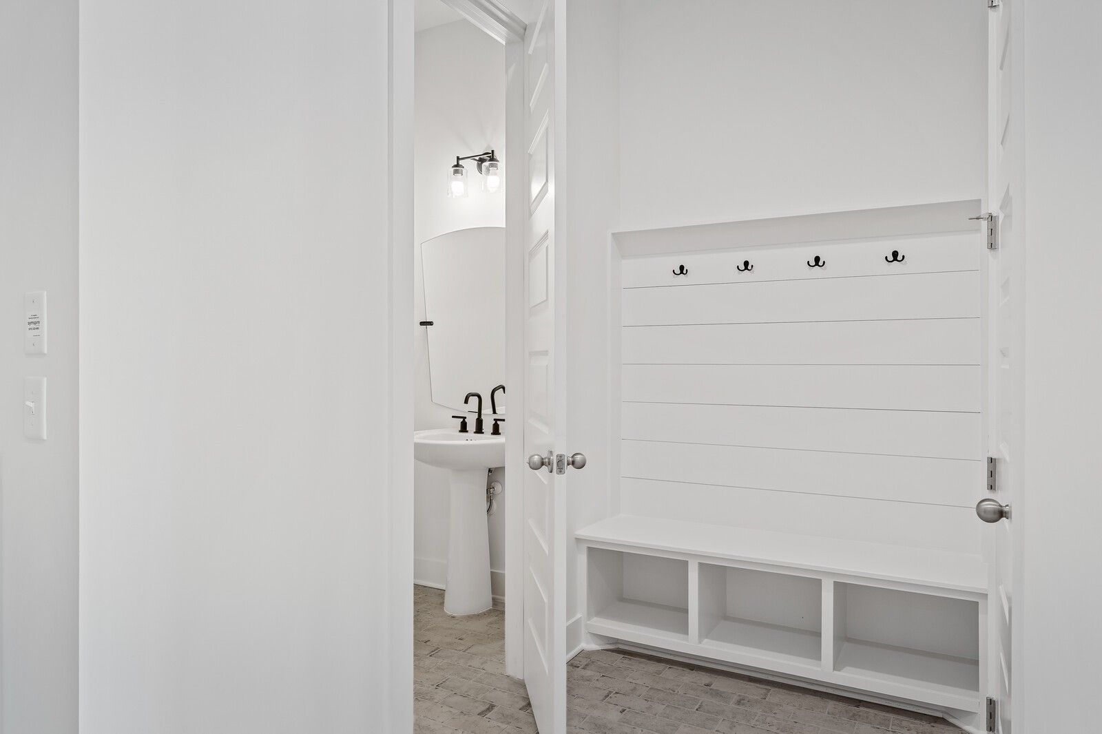 White shiplap mudroom with built-in bench, coat hooks, and adjacent powder room sink in Davidson Homes The Alston A, Murfreesboro