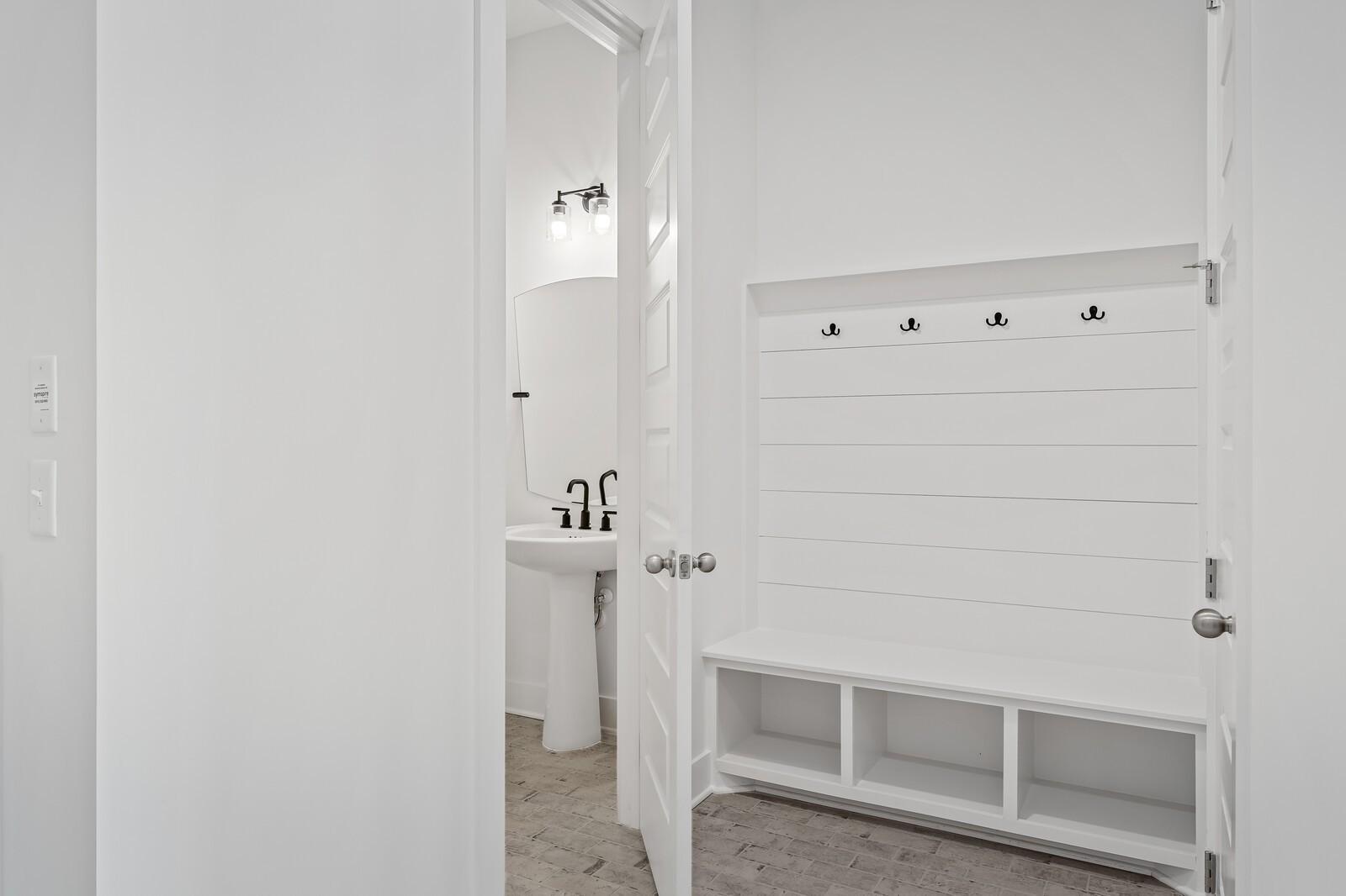 White shiplap mudroom with built-in bench, coat hooks, and adjacent powder room sink in Davidson Homes The Alston A, Murfreesboro