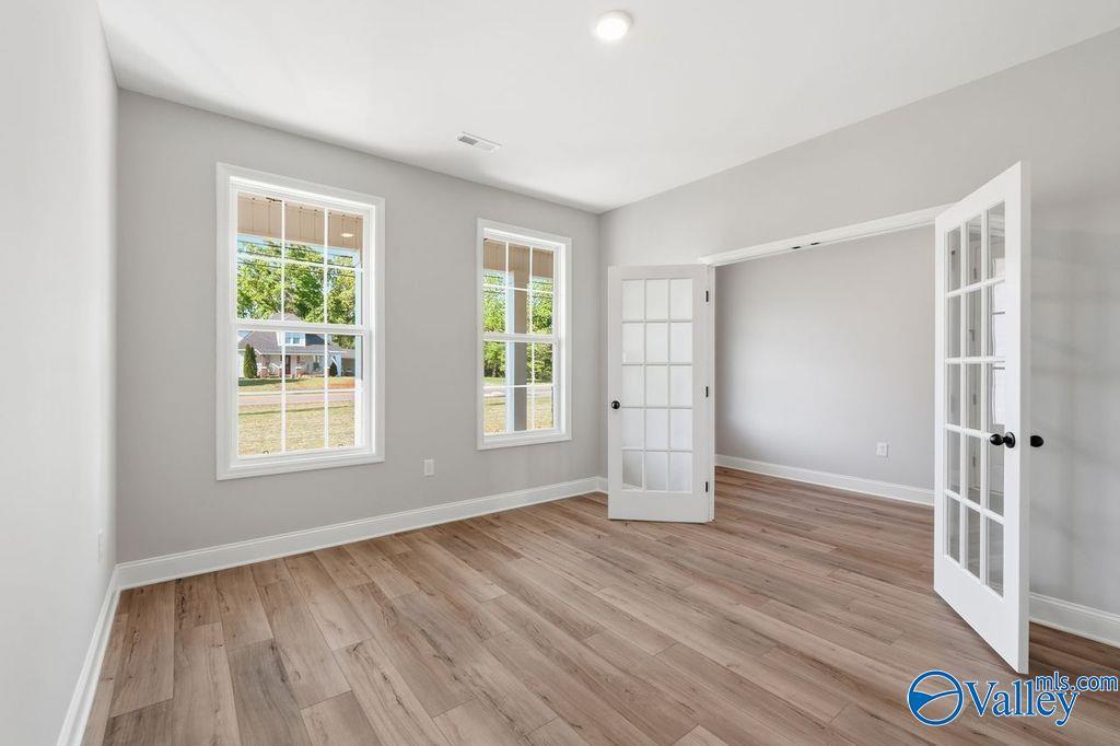 Bright room with light gray walls, hardwood floors, open French doors, and backyard views through large windows in Davidson Homes The Emory, Decatur AL