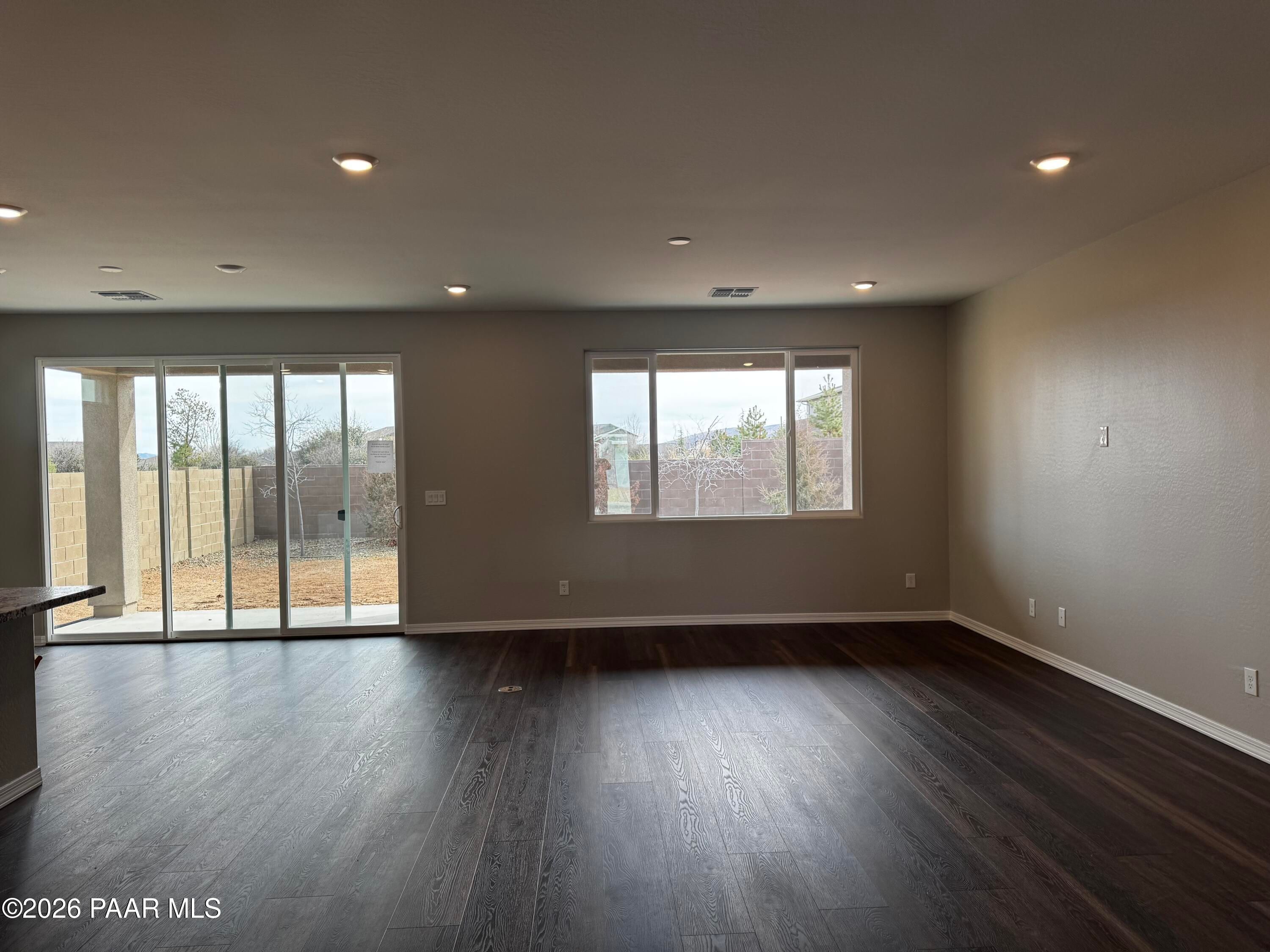 Spacious living room with beige walls, dark hardwood floors, and sliding doors to fenced backyard in Durango II B, Westwood, Prescott, AZ