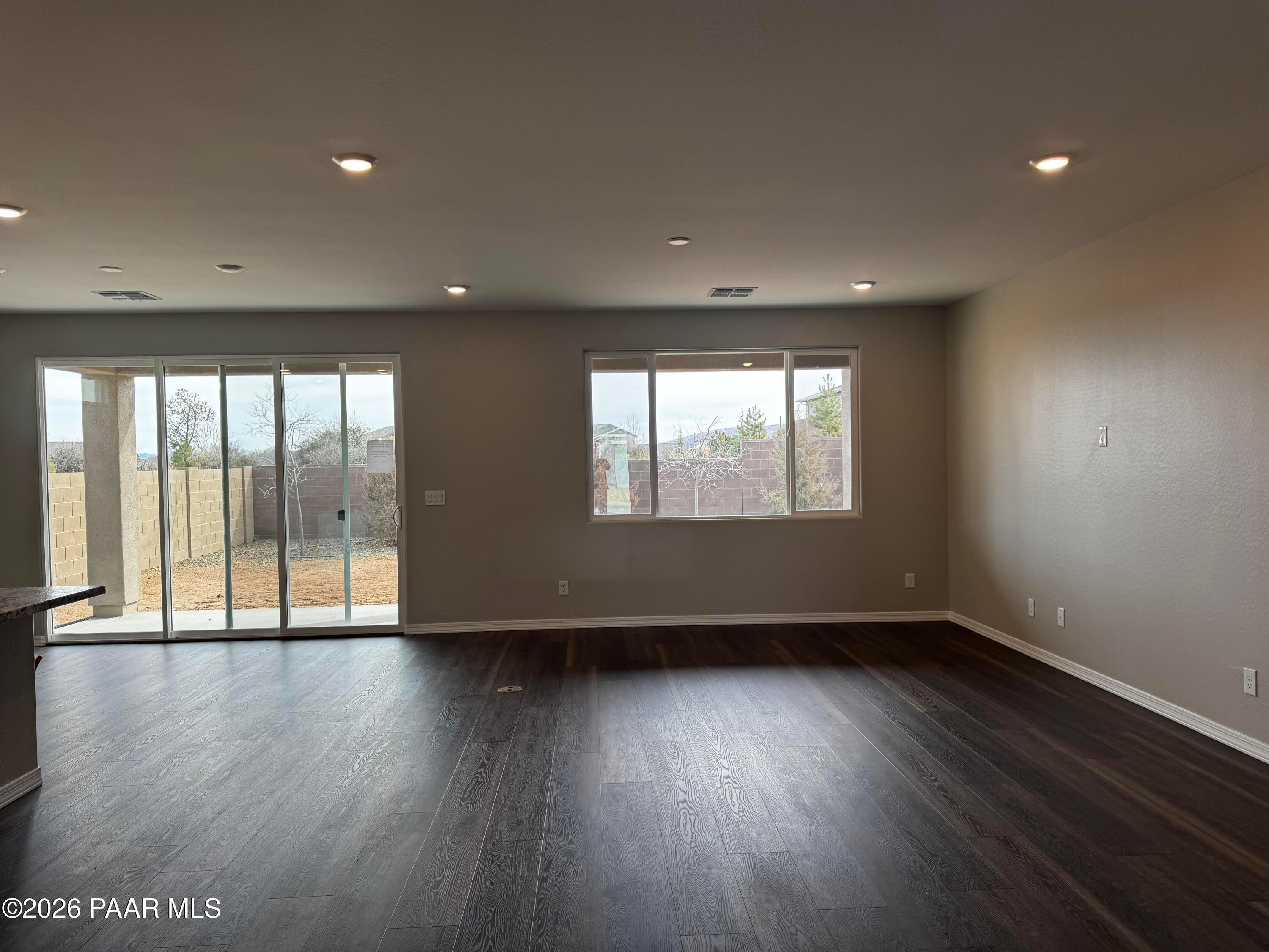Spacious living room with beige walls, dark hardwood floors, and sliding doors to fenced backyard in Durango II B, Westwood, Prescott, AZ