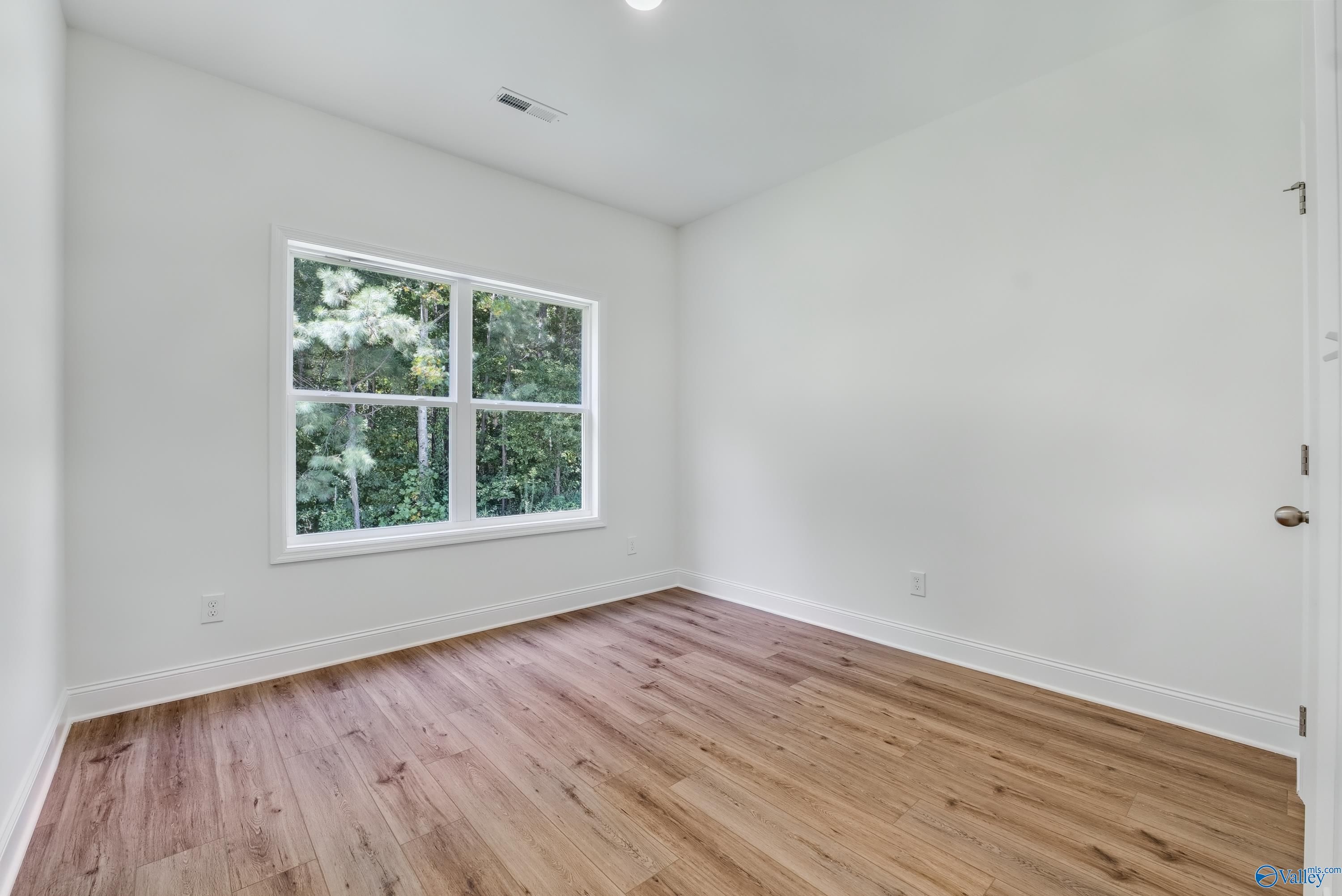 Bright secondary bedroom with hardwood floors and large window view of trees in Davidson Homes The Shelby A, Arab, Alabama