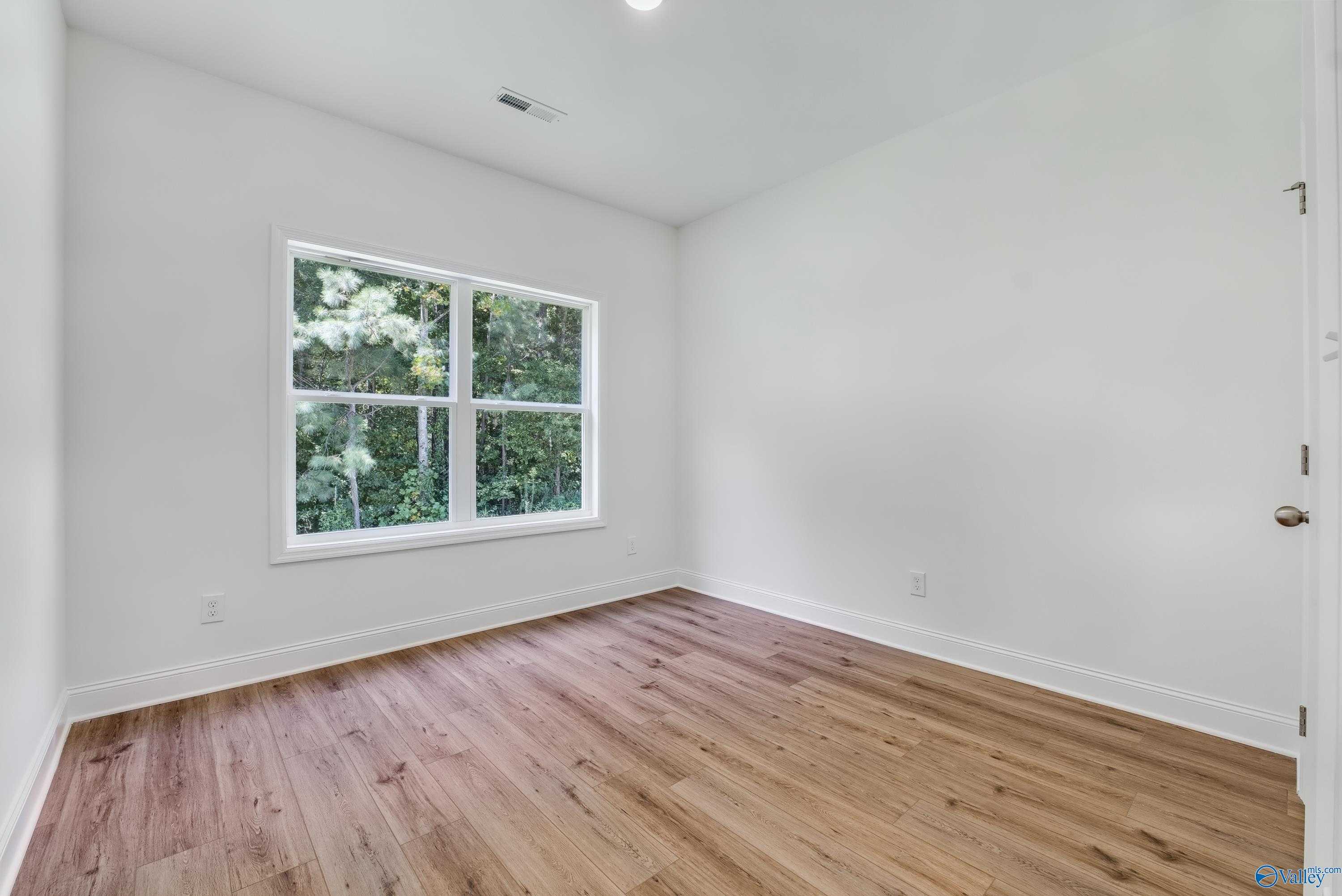 Bright secondary bedroom with hardwood floors and large window view of trees in Davidson Homes The Shelby A, Arab, Alabama