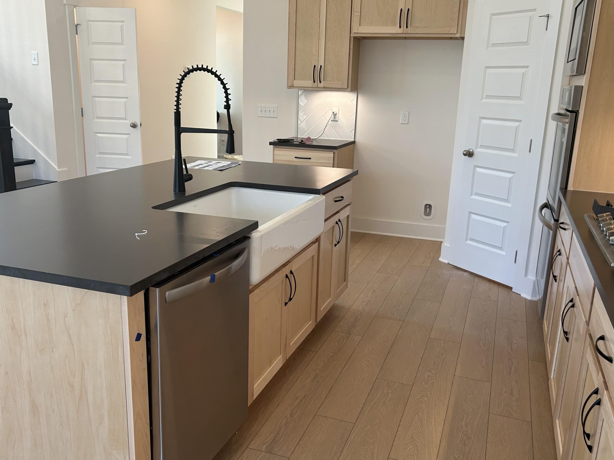 Modern kitchen featuring white farmhouse sink, black granite island, light wood cabinets in Davidson Homes The Ridgeport E, Mt. Juliet
