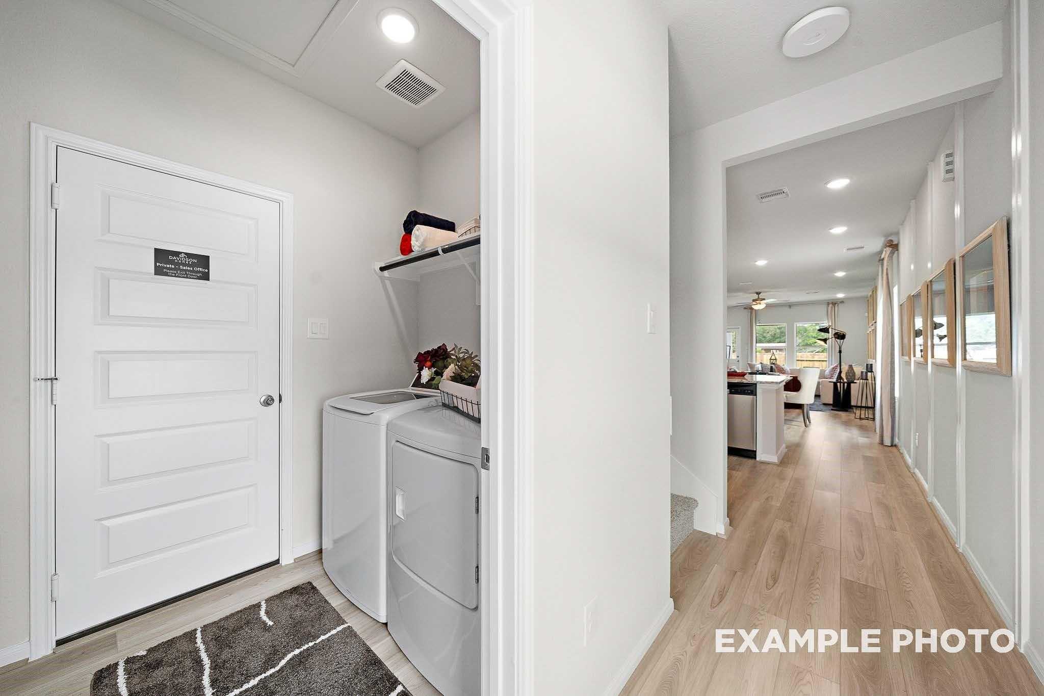 Bright laundry room with white washer dryer and open shelves opening to hardwood hallway in Davidson Homes San Marcos E, Conroe TX