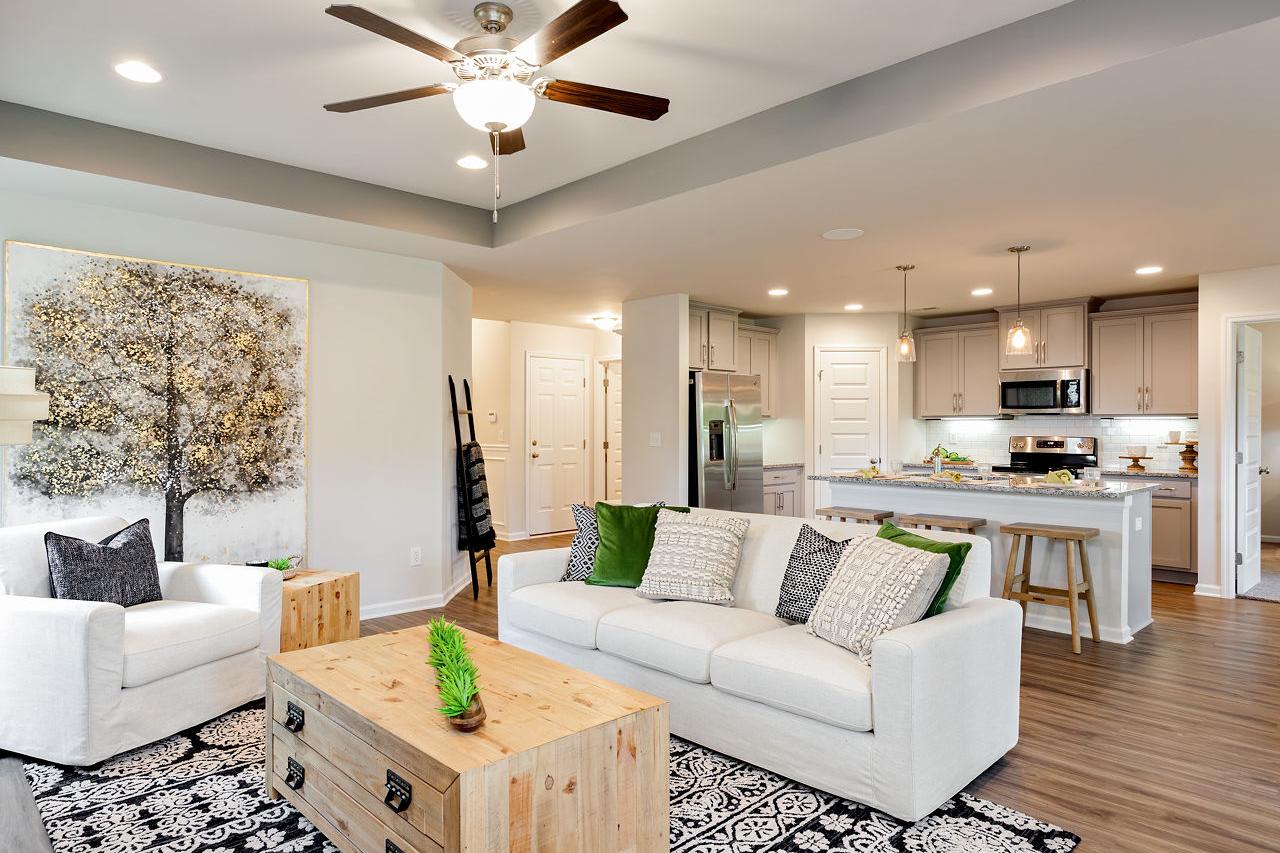 Spacious open-concept living room in The Franklin C with white sectional sofa, wooden coffee table, abstract tree art, and adjacent kitchen island