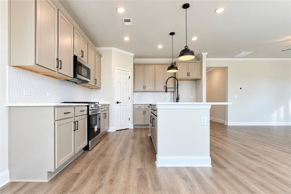 Modern open-concept kitchen with taupe shaker cabinets, white island, and black pendant lights in Davidson Homes The Harrison H plan