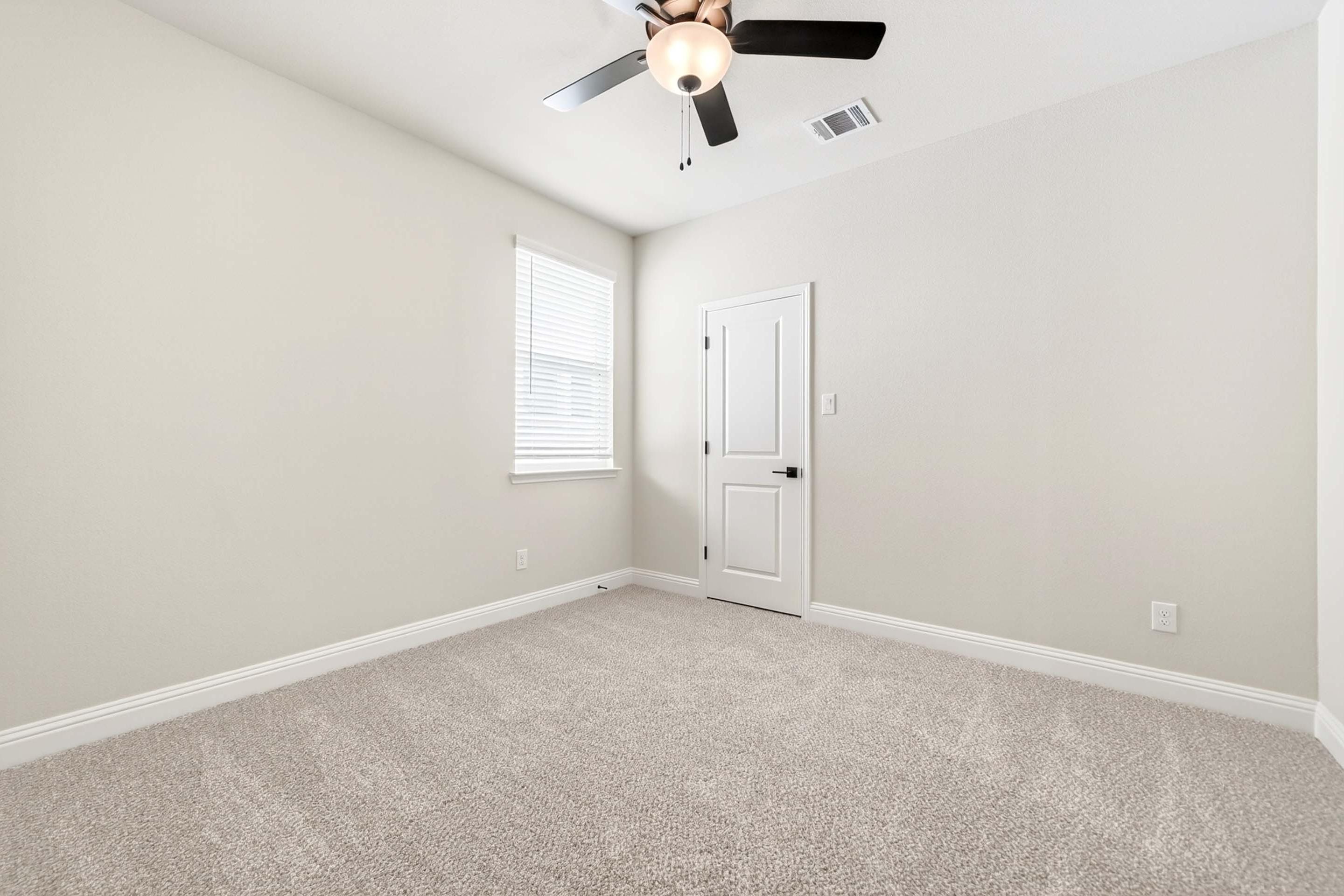 Spacious secondary bedroom in The Holly floor plan featuring neutral carpet, white walls, and a ceiling fan.