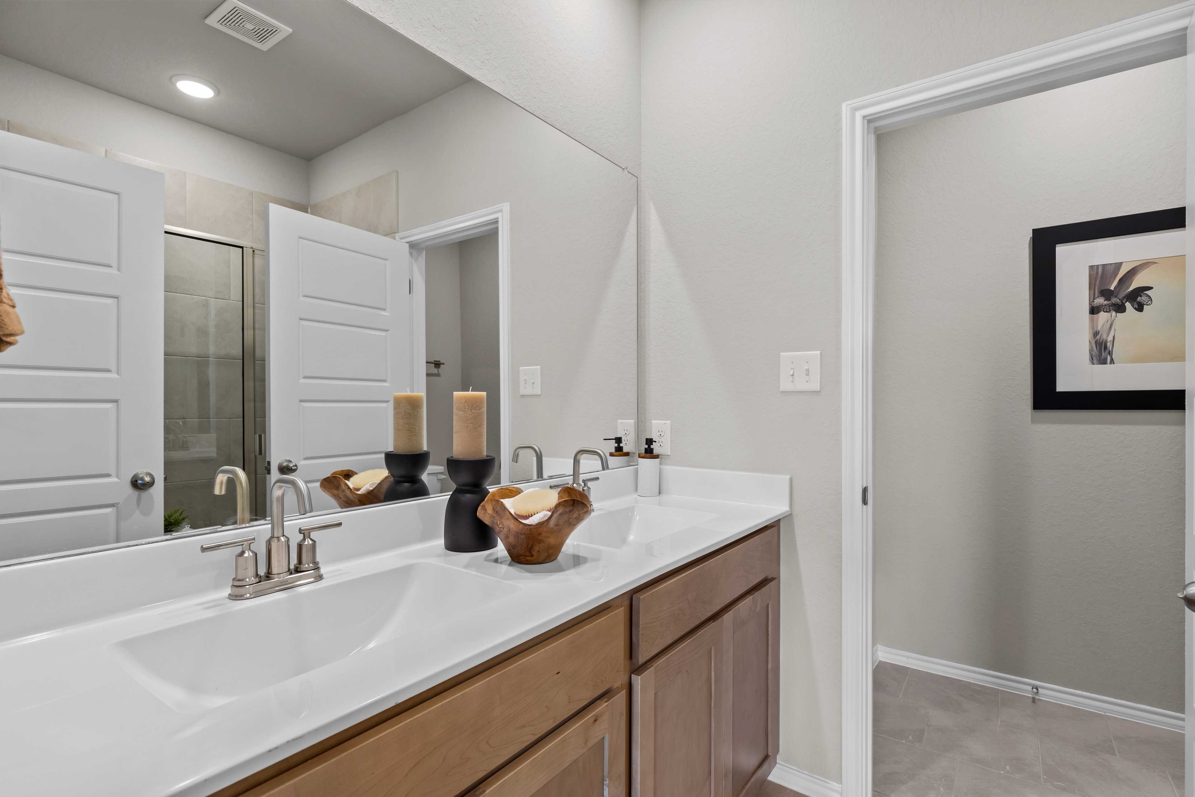 Spacious master bathroom in The Sabine C with double vanity, light wood cabinets, large mirror, and glass shower