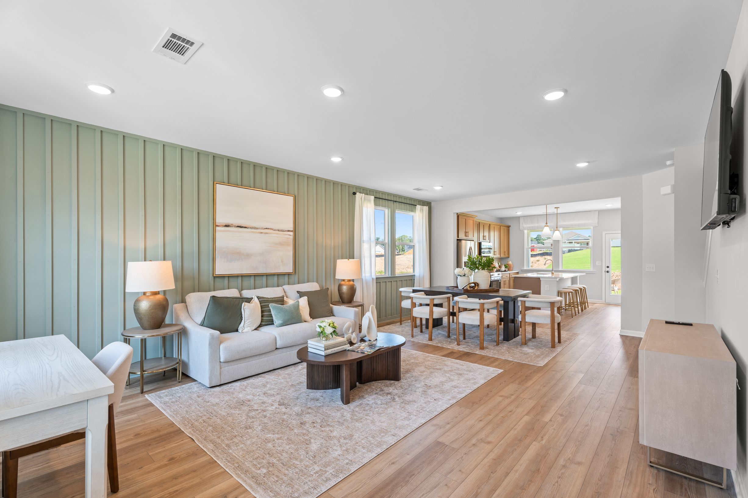 Open-concept living and dining area at Links Crossing in Auburn, Alabama by Davidson Homes with sage green accent wall.