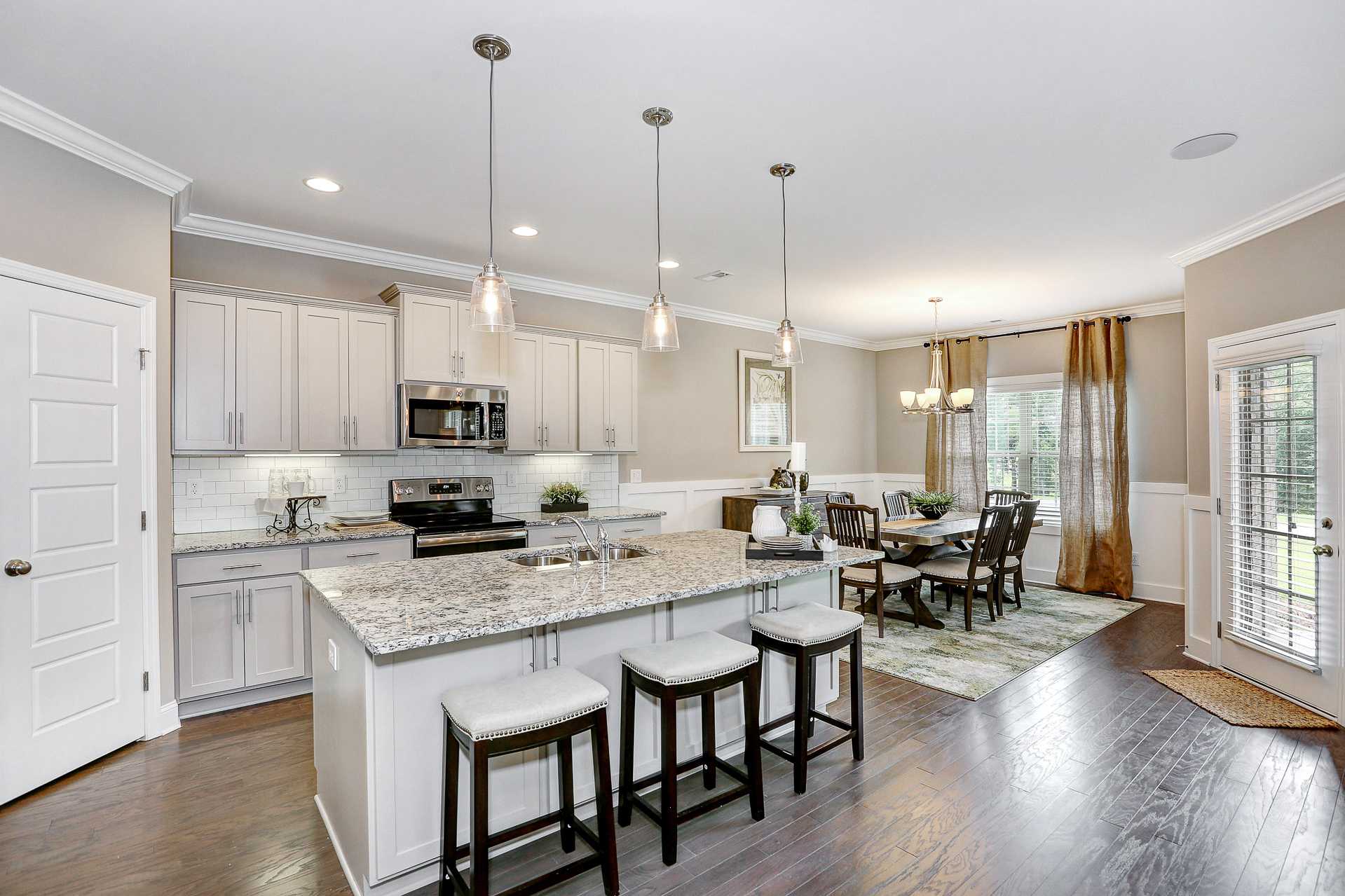 Spacious open-concept kitchen dining area Stone Creek Phase II Cullman AL white shaker cabinets granite island hardwood floors pendant lights