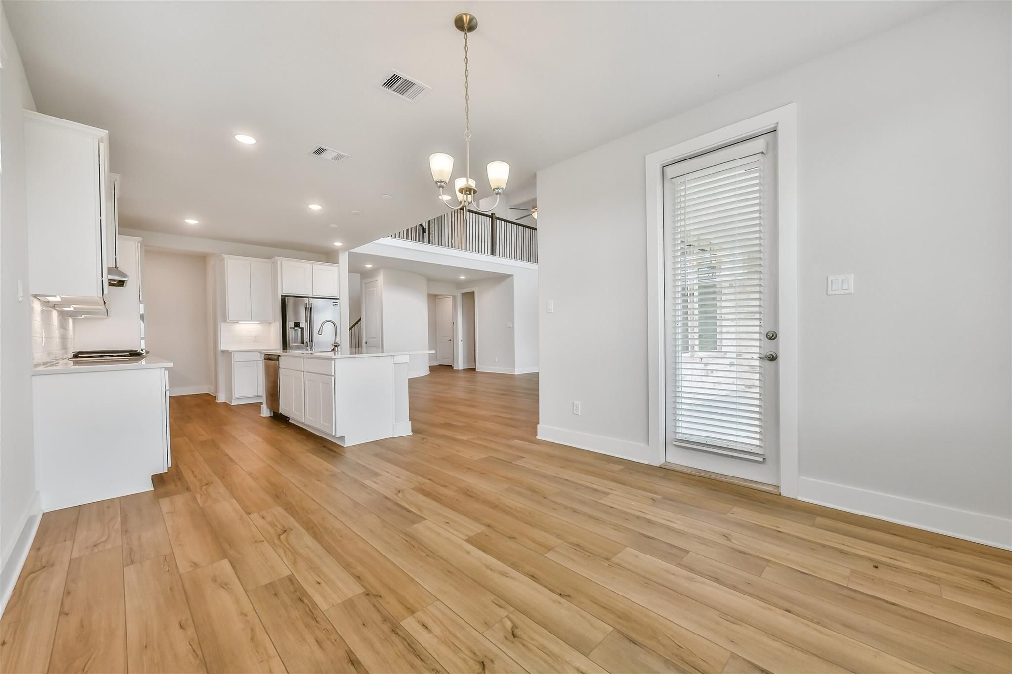 Open-concept kitchen with white cabinets, large island sink, stainless appliances, and oak hardwood floors overlooking loft balcony in Davidson Homes Victoria A, Lago Mar