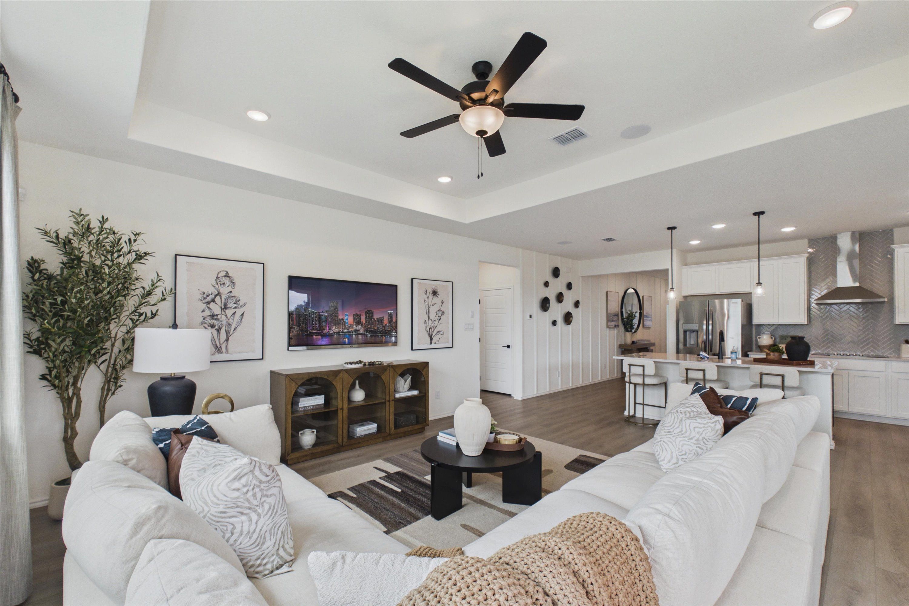 Open-concept living room and kitchen in Rayburn Valley, San Antonio TX by Davidson Homes with white sectional sofa, ceiling fan, and modern island