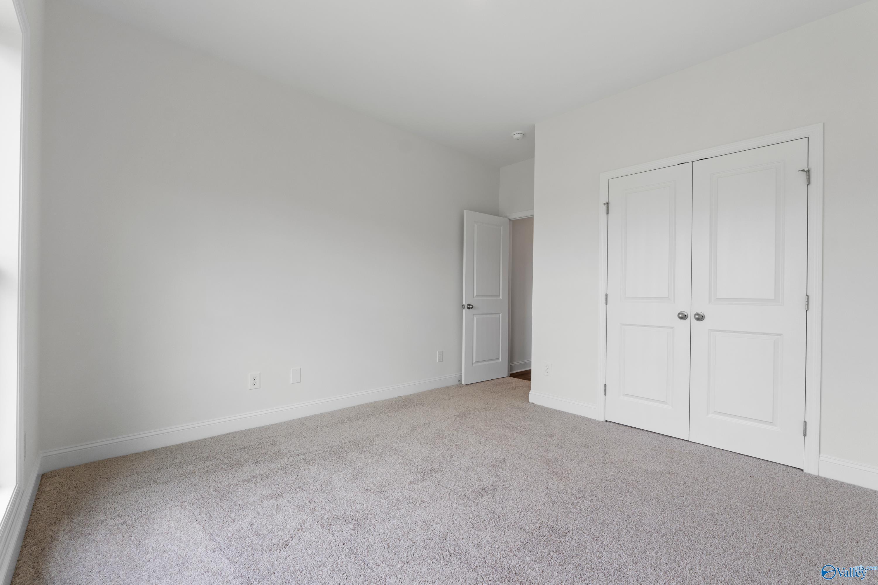 Bright bedroom with neutral carpet and double closet in The Everett B floor plan at The Meadows, Athens, Alabama.