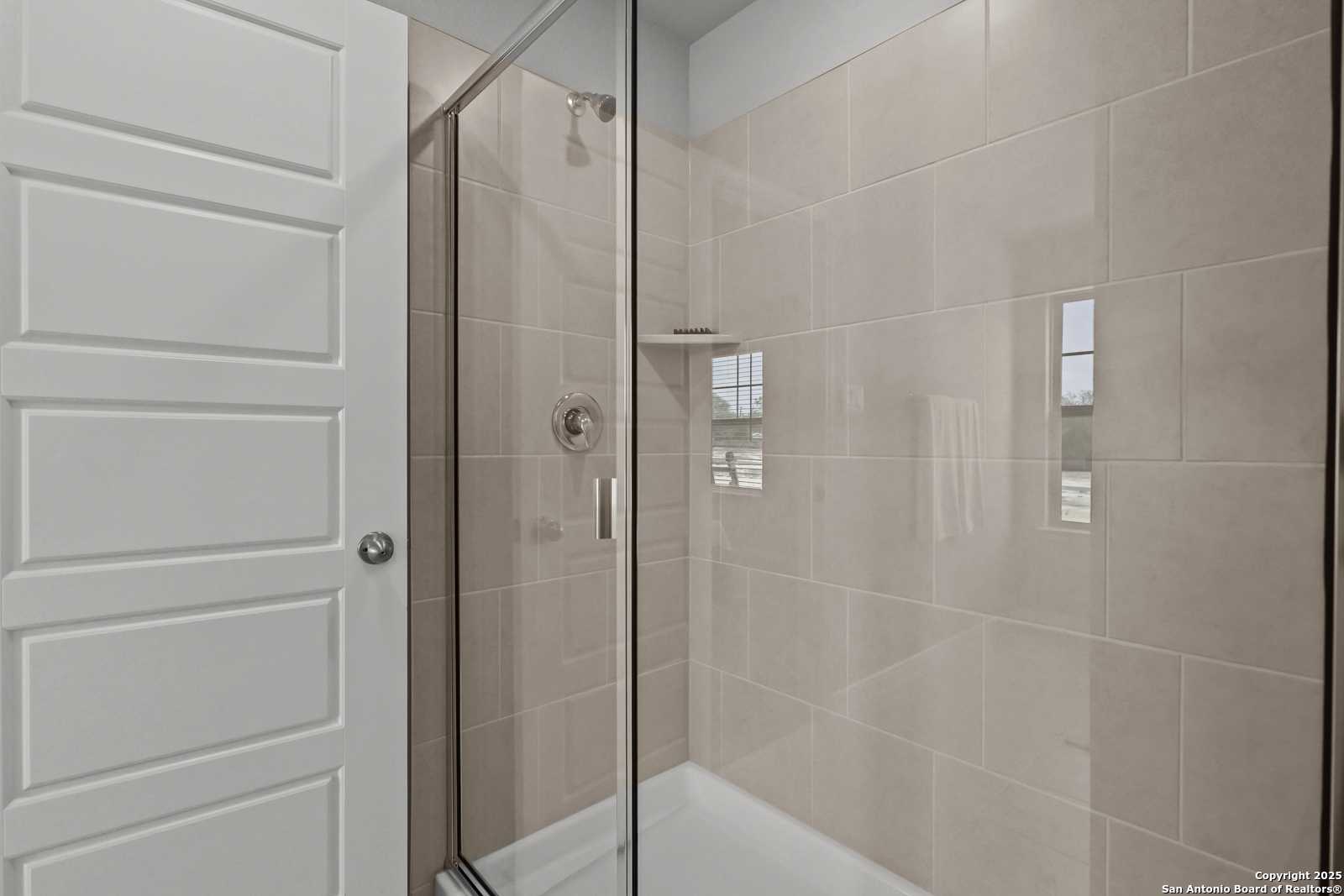 Elegant bathroom with glass shower enclosure, beige tiles, and tub in Davidson Homes The Gillian C, San Antonio, Texas