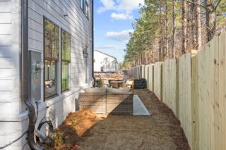 The Washington H townhome side exterior with white siding, large windows, fenced patio, and pine trees in Marietta