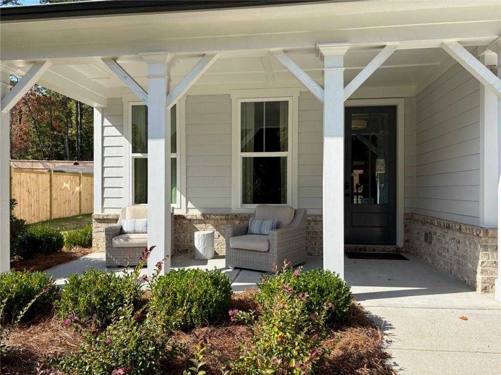 Welcoming covered front porch with white columns, cushioned chairs, and lush shrubs on Davidson Homes The Hickory B in Riverwood, Dallas, Georgia