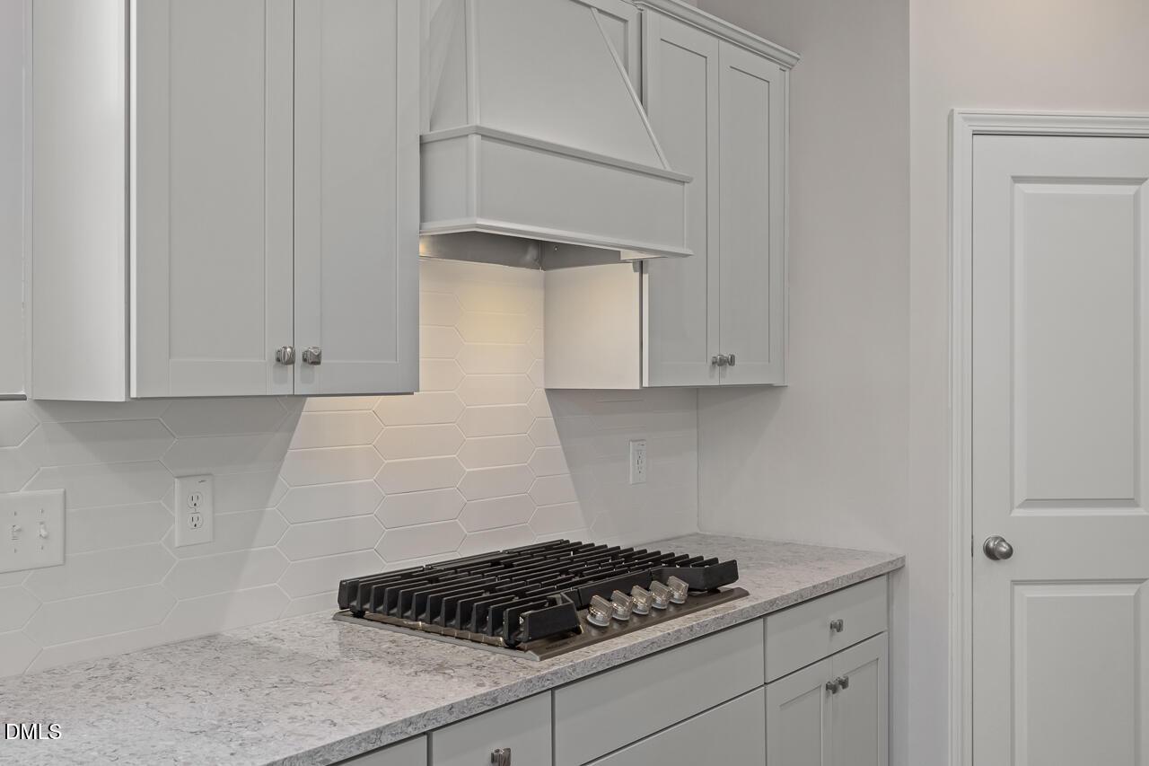 Modern kitchen with gas cooktop, light gray cabinets, and white tile backsplash in The Ashport G at Sage on North Main.