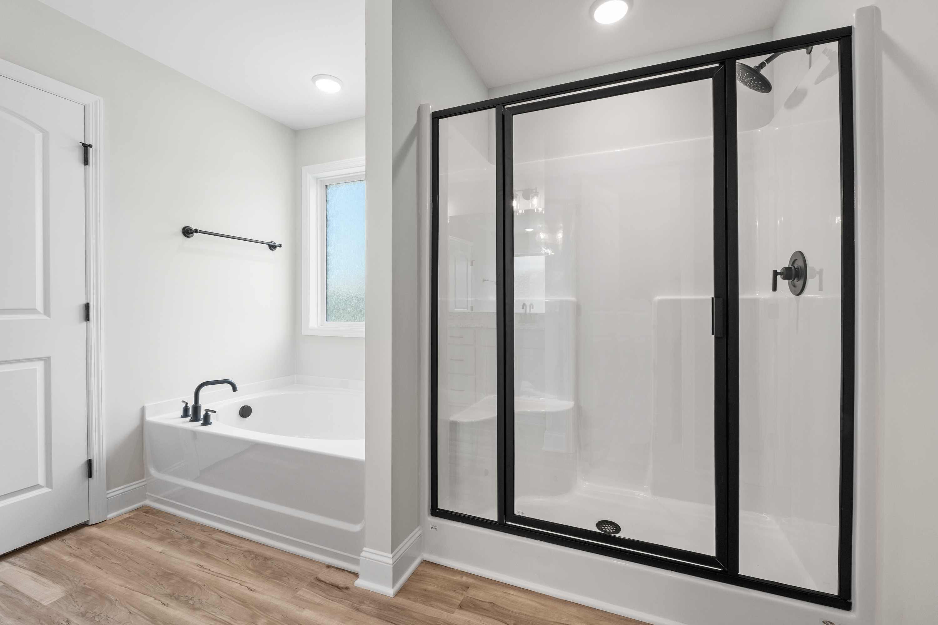 Spacious master bathroom in The Everett featuring freestanding soaking tub, black-framed glass shower, and modern fixtures