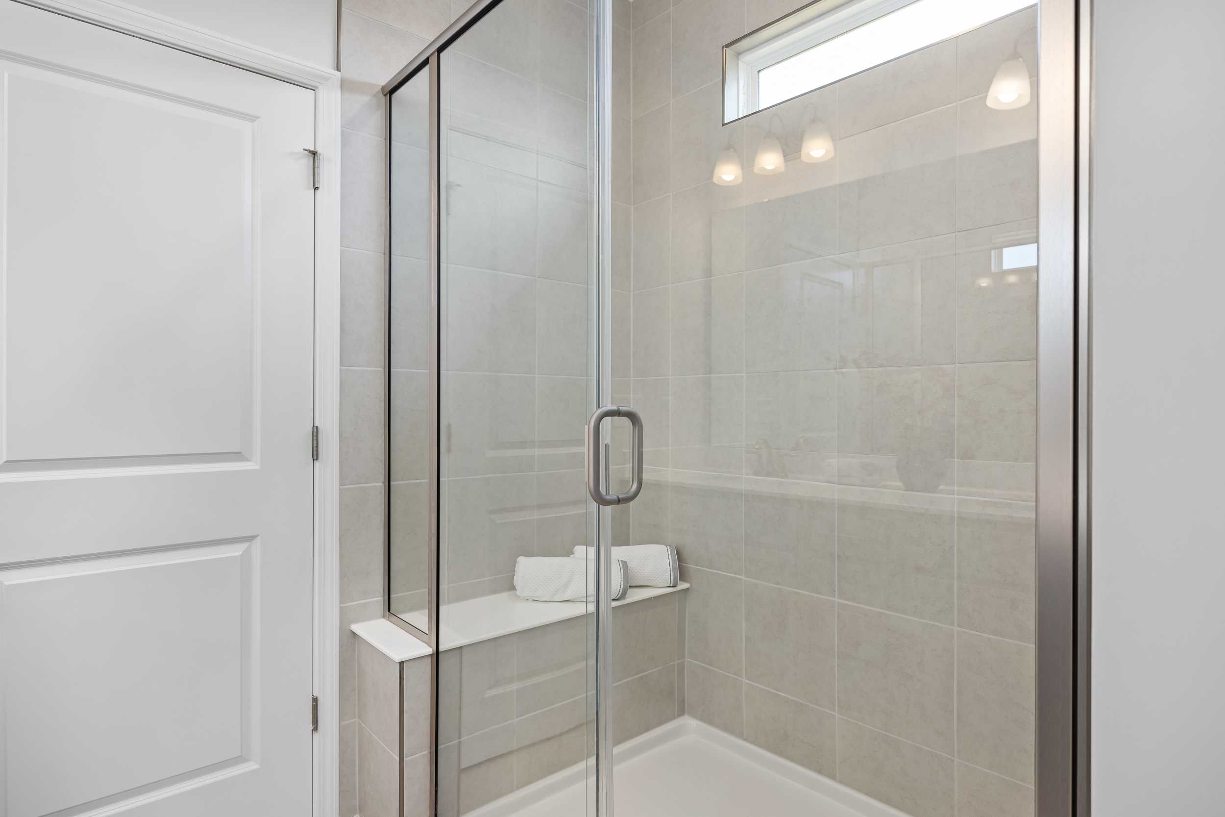 Spacious glass walk-in shower in The Daphne C master bathroom with tiled walls, built-in bench, and folded white towels