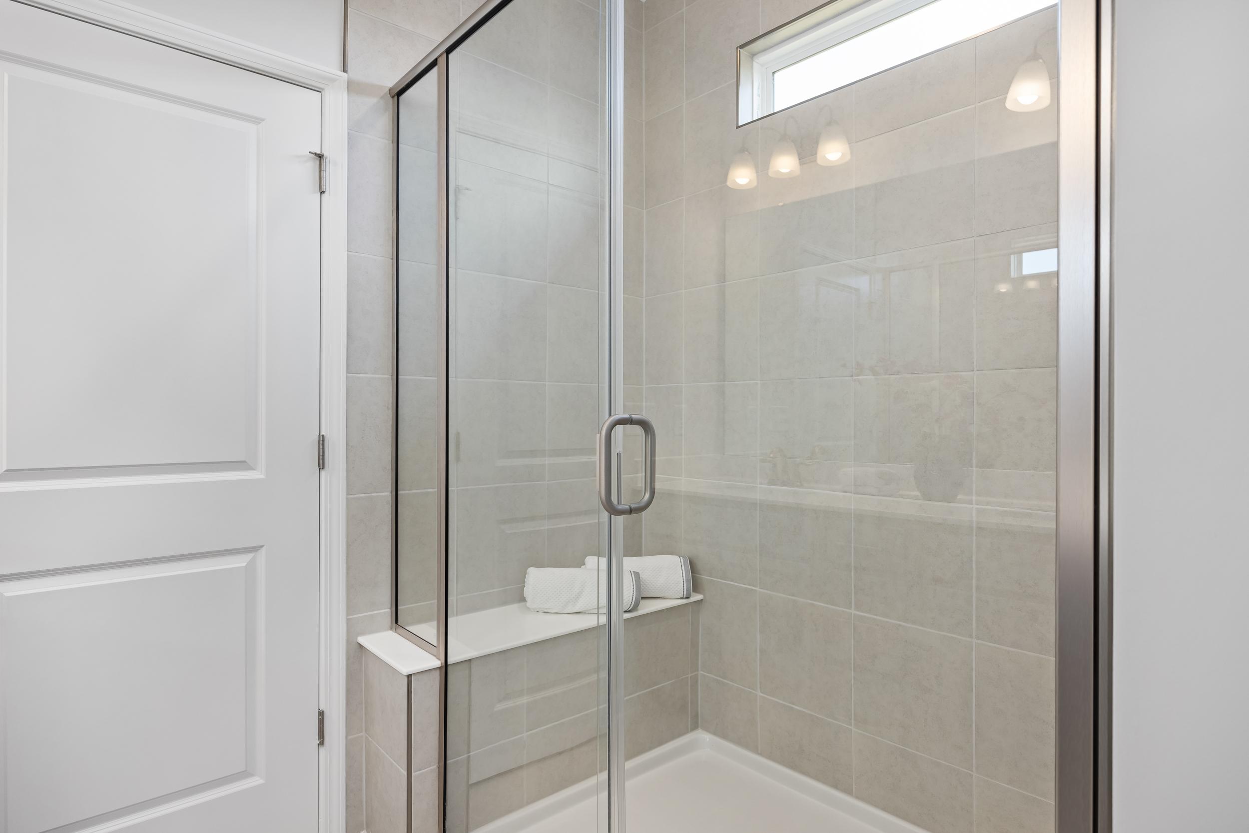 Spacious walk-in shower in The Daphne D master bathroom with frameless glass doors, tiled walls, bench seating, and recessed lighting