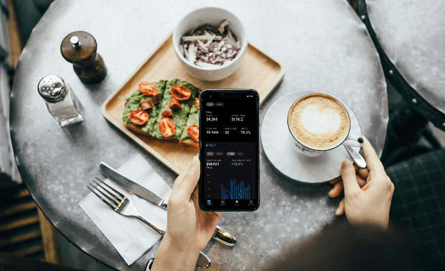 Person sitting in front of food holding a smartphone showing the InCharge mobile app - restaurant reporting and analytics - SkyTab