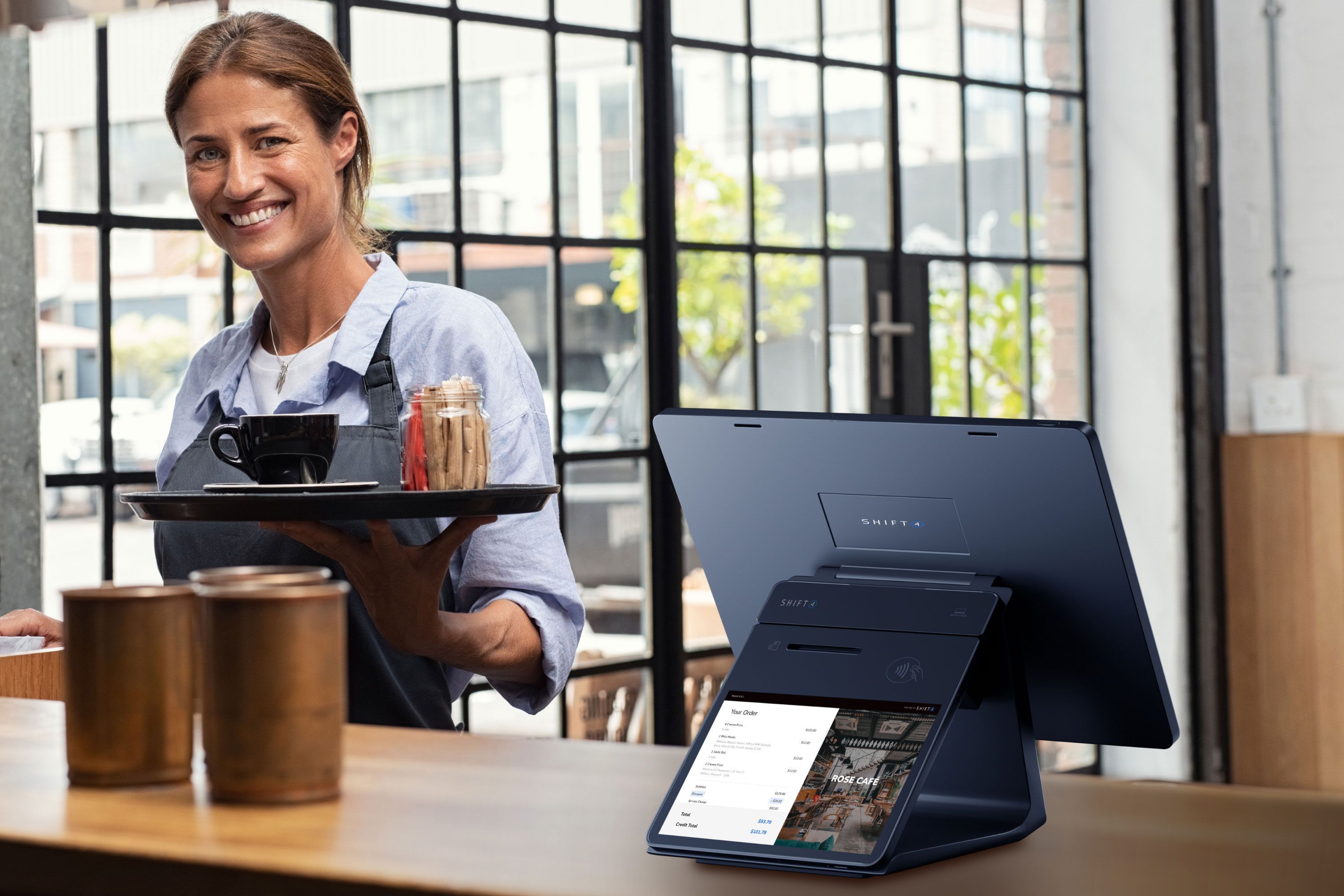 Smiling restaurant employee holding a platter and standing next to a SkyTab POS system with a Customer-Facing Display - coffee shop POS system - SkyTab