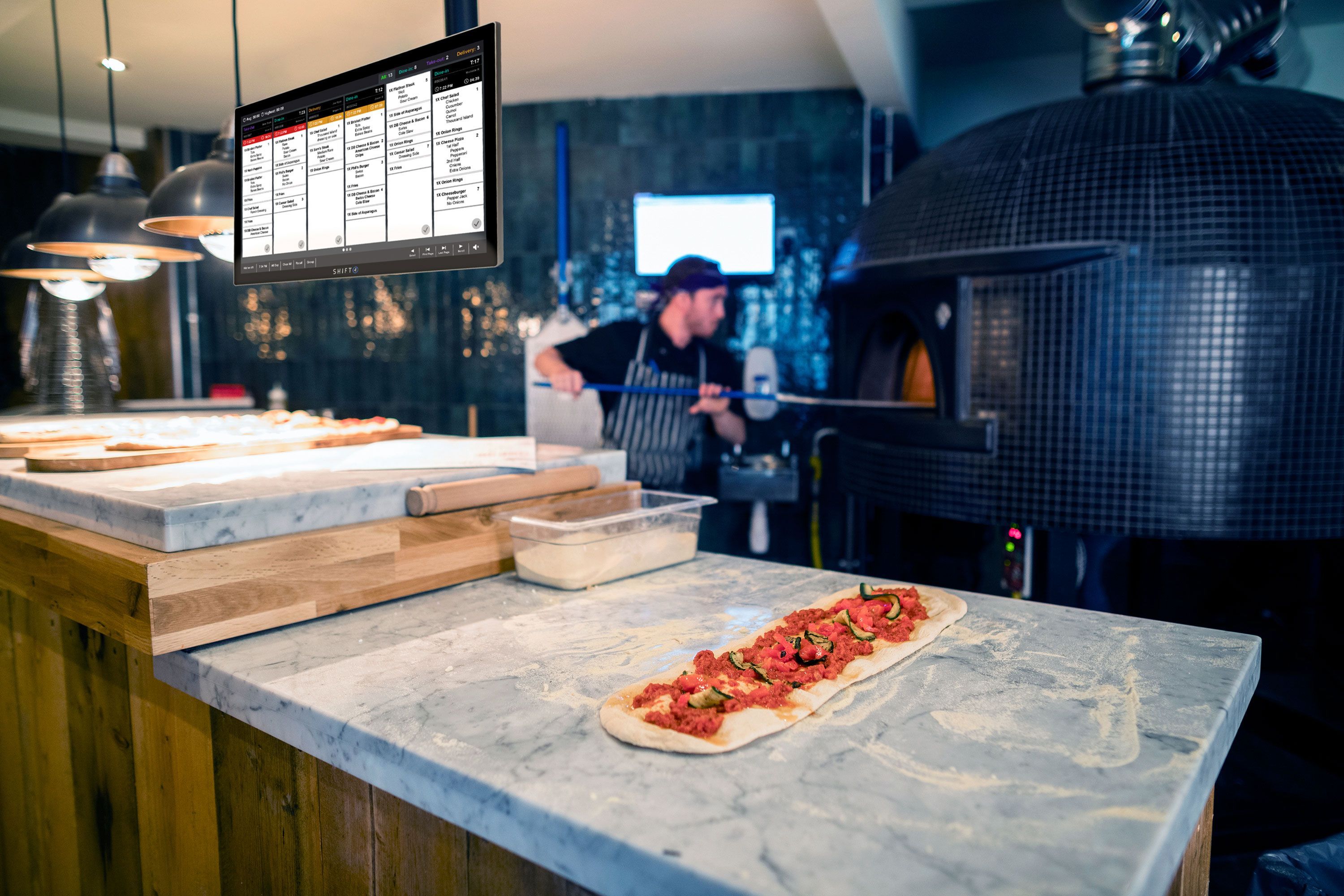 Restaurant employee using a brick oven while a SkyTab Kitchen Display system hands in the foreground - SkyTab