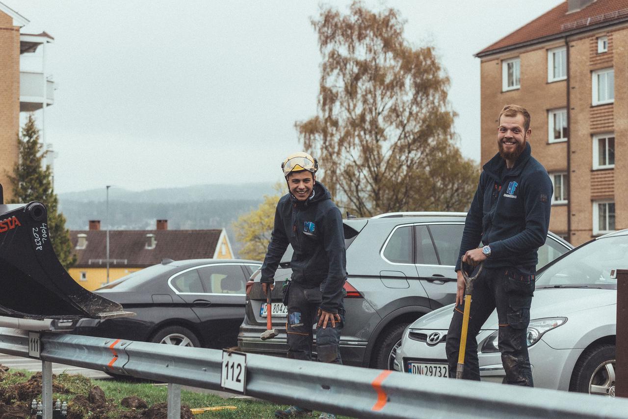 To montører, der smiler på en parkeringsplads udenfor en lejlighed.