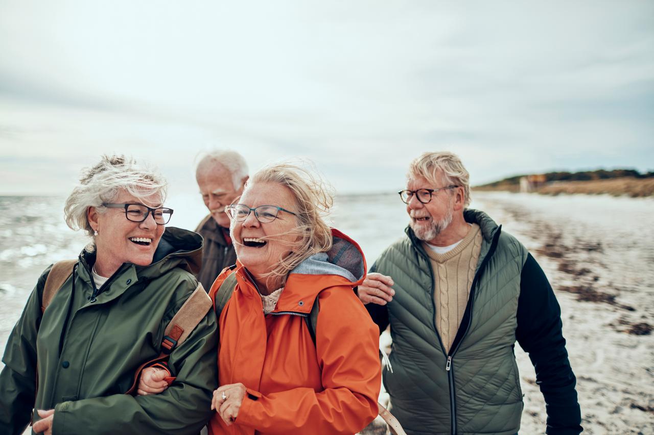 Billede af 4 ældre mennesker, der går en tur på en strand og smiler og ler