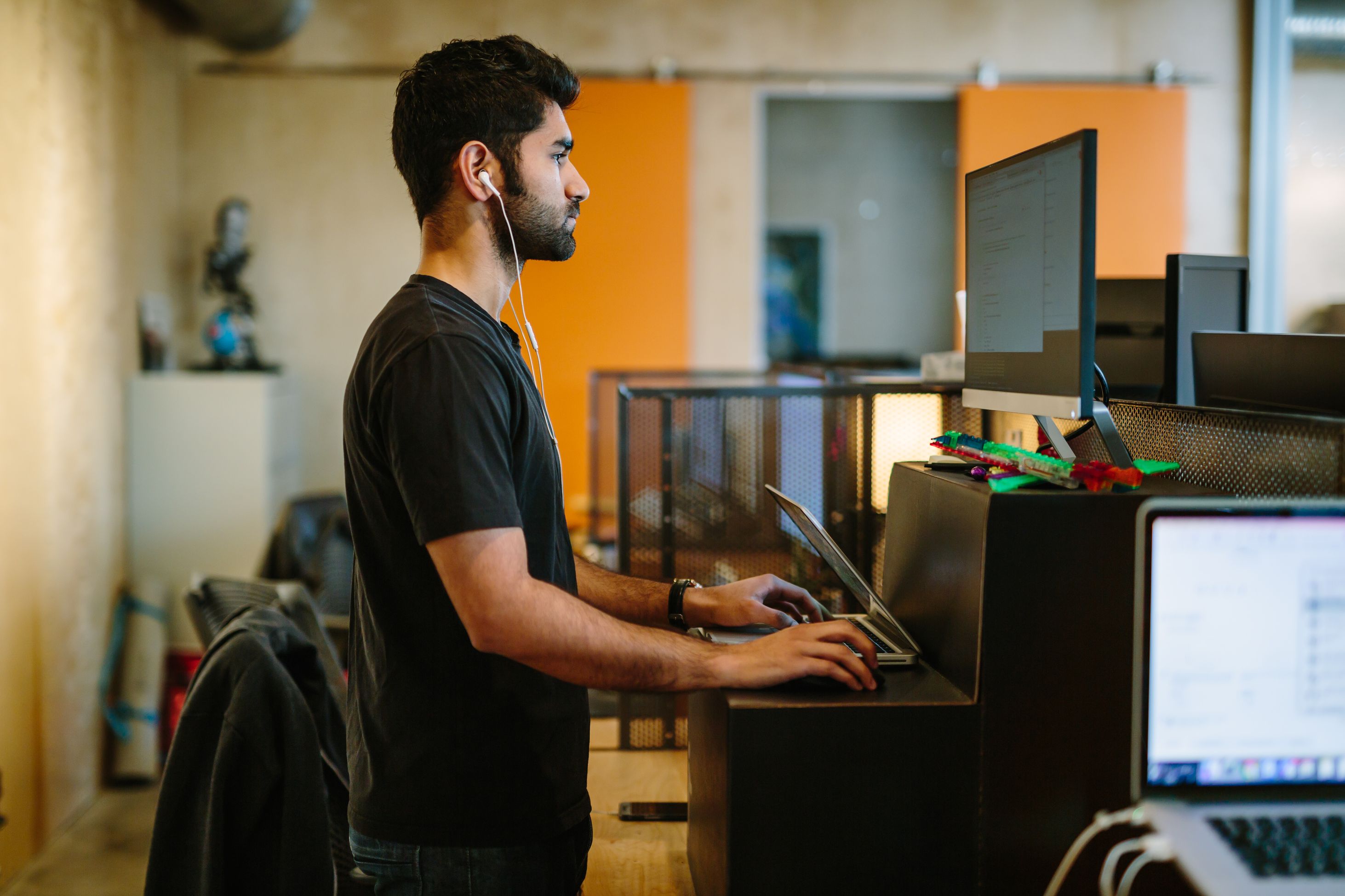 man writing code at a standing desk with laptop and external monitor