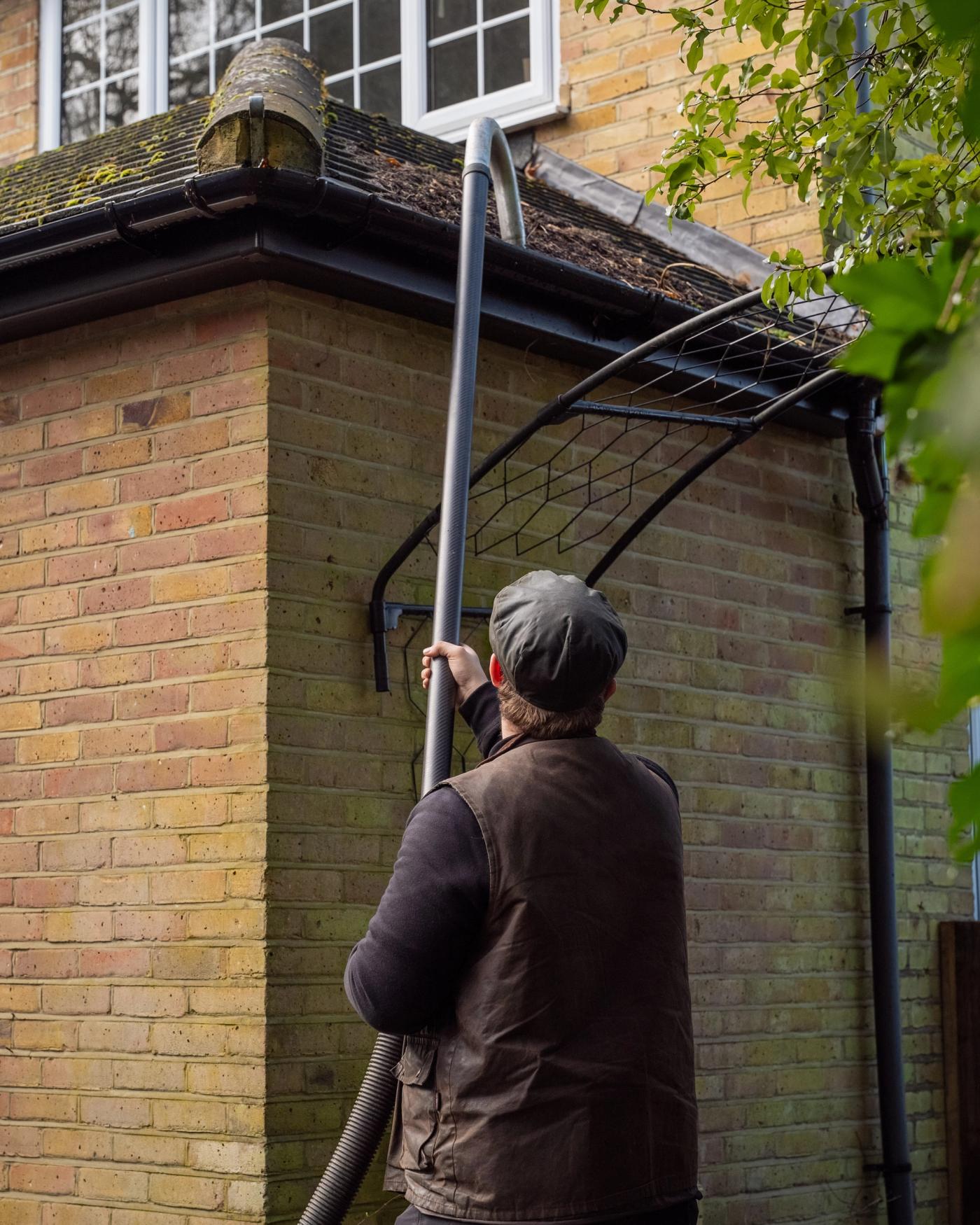 A high-suction SkyVac gutter clearing pole reaching the roofline of a well-kept Kent home, with the operator working safely from the ground beside clipped hedging