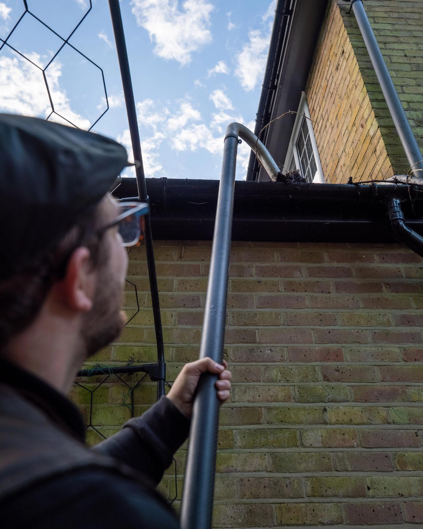 A close exterior view of a London townhouse roofline with leaves and moss visible in the gutter, rainwater spilling over a small section during wet weather
